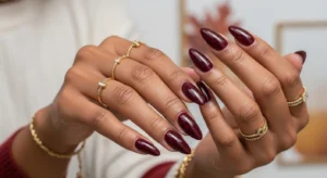 Deep burgundy fall nails on dark skin with glossy finish and almond shape