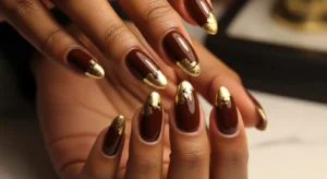 Brown nails with gold foil design on dark skin for fall
