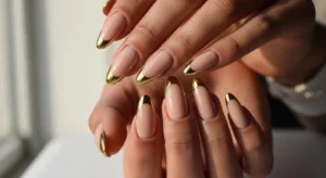 Nude nails with gold chrome tips on deep skin tone, elegant style