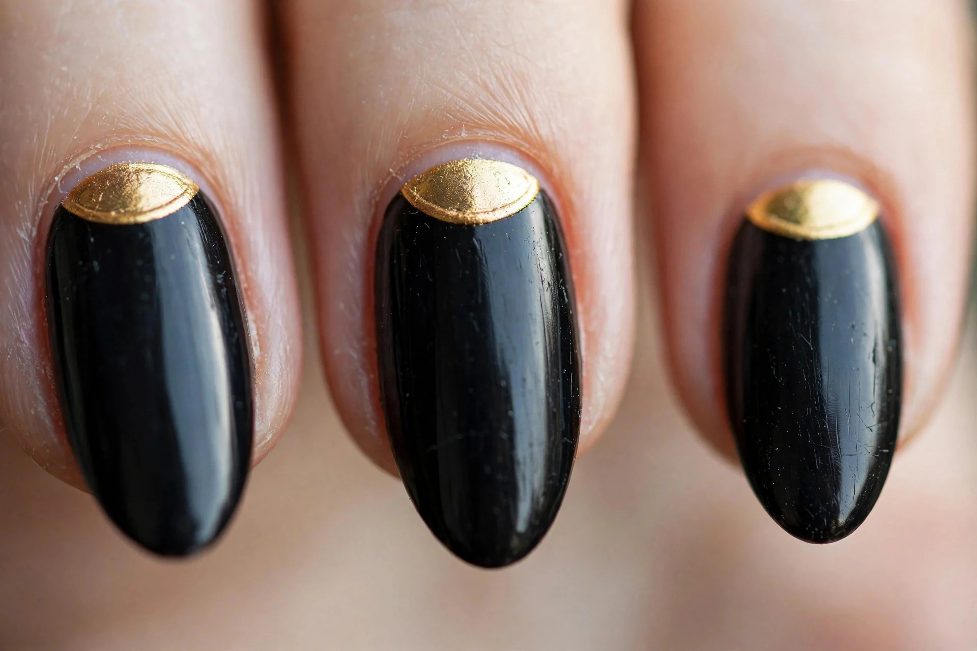 Almond nails in black polish with a gold half-moon at the cuticle