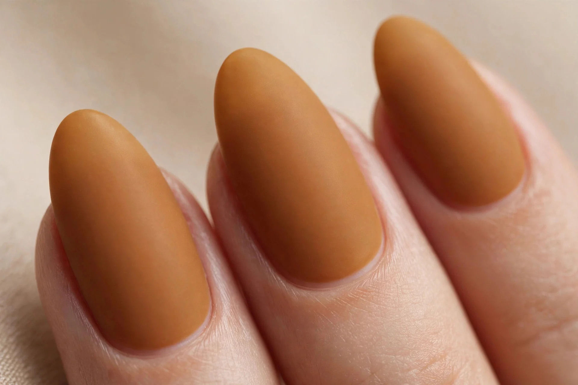 Almond nails in matte spiced amber polish, soft beige background