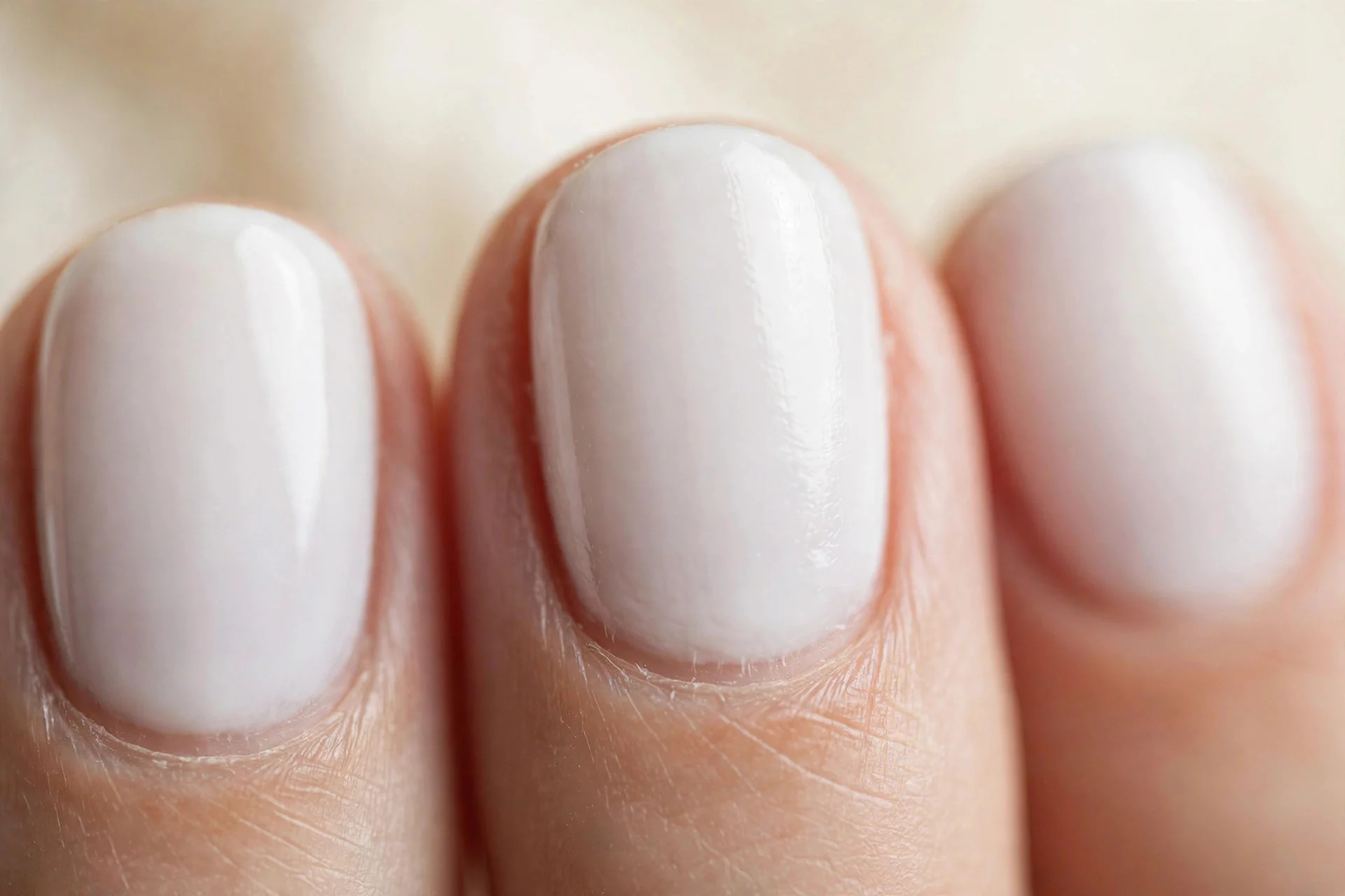 Milky white opaque polish on short oval nails, soft and glossy, cream background