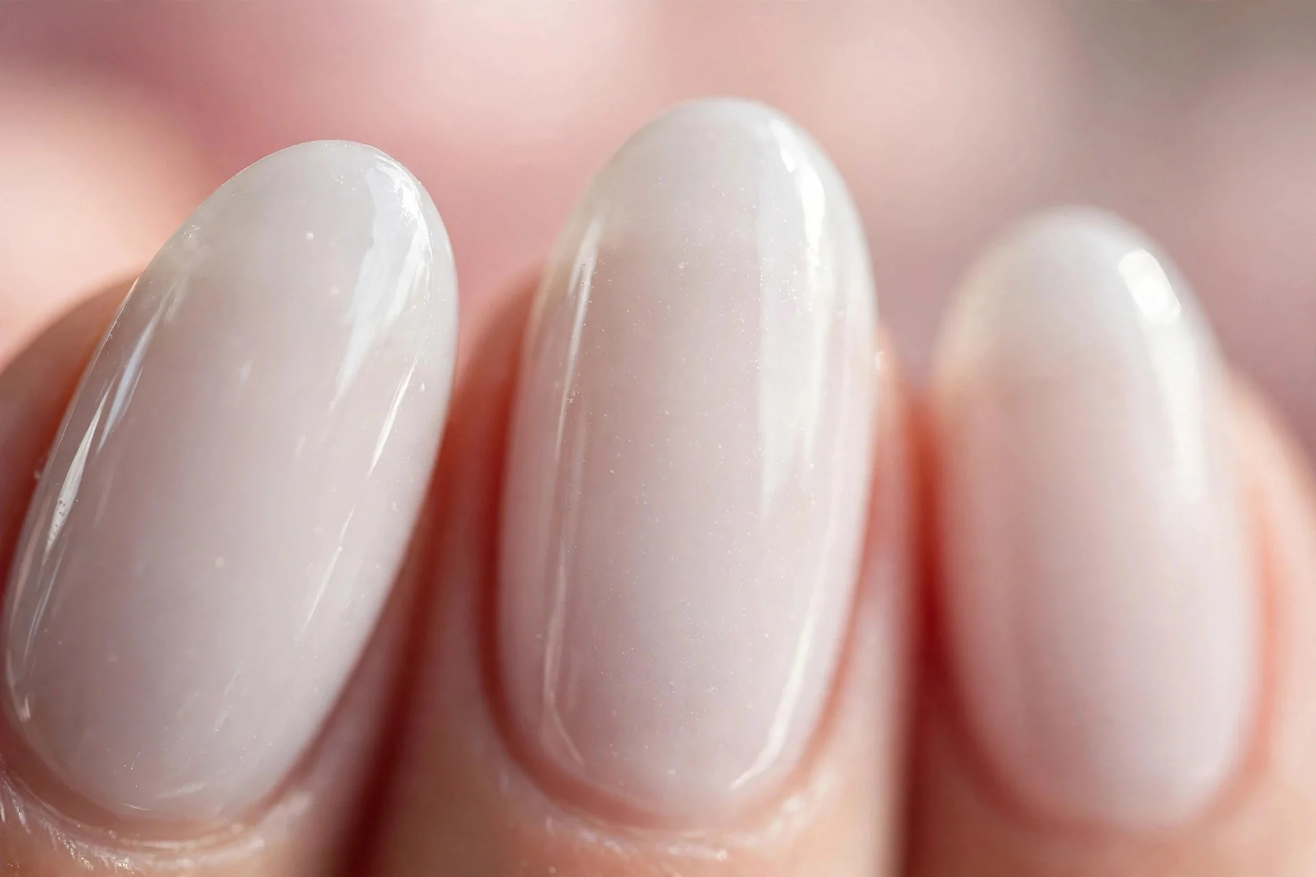 Sheer milky white polish on medium almond nails, soft and glossy, blush background