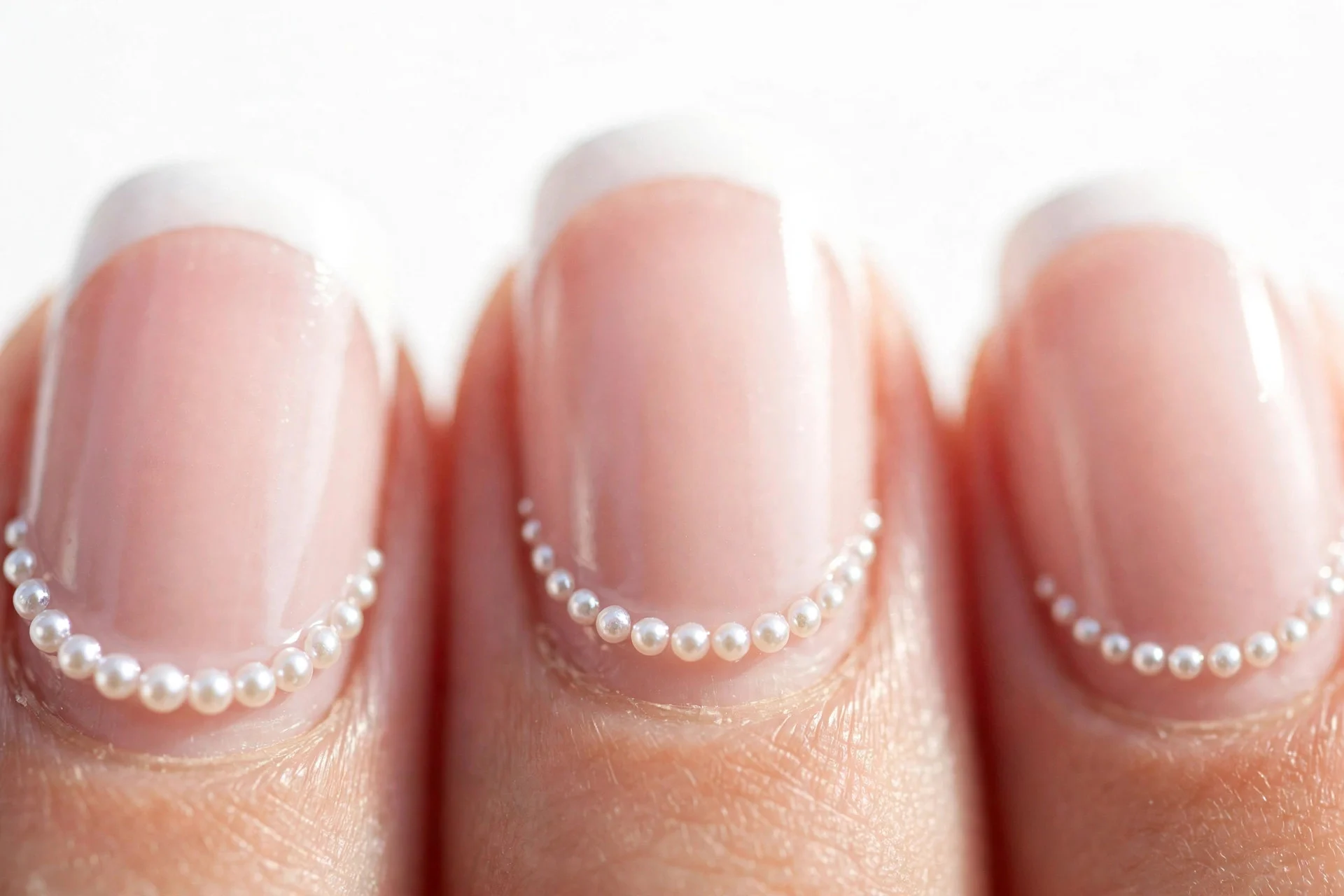 Classic French nails with tiny pearls dotted along the smile line, glossy, white background