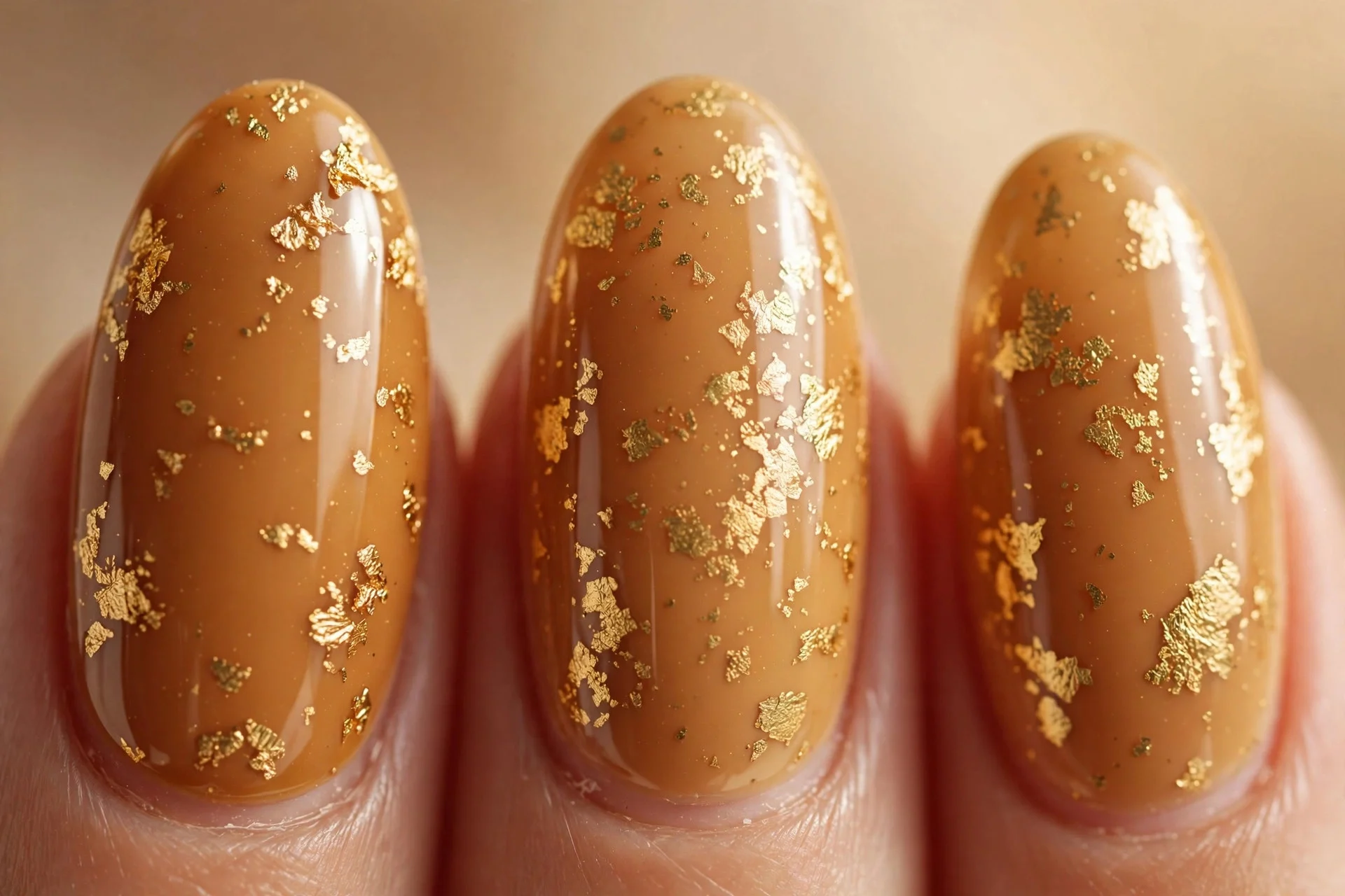 Almond nails in honeyed caramel with gold foil flakes, warm background