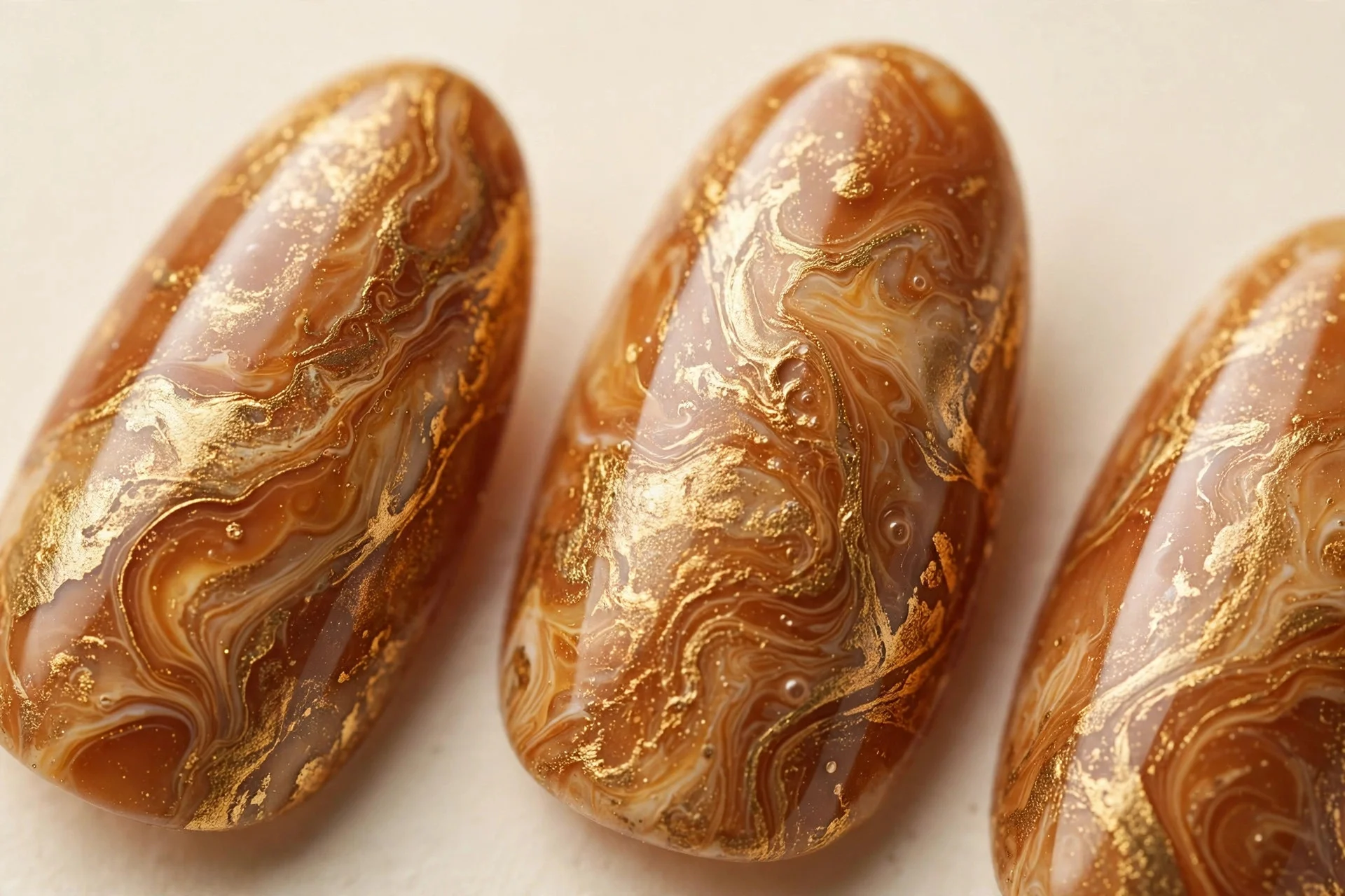 Almond nails with toffee caramel and gold marble pattern, cream background