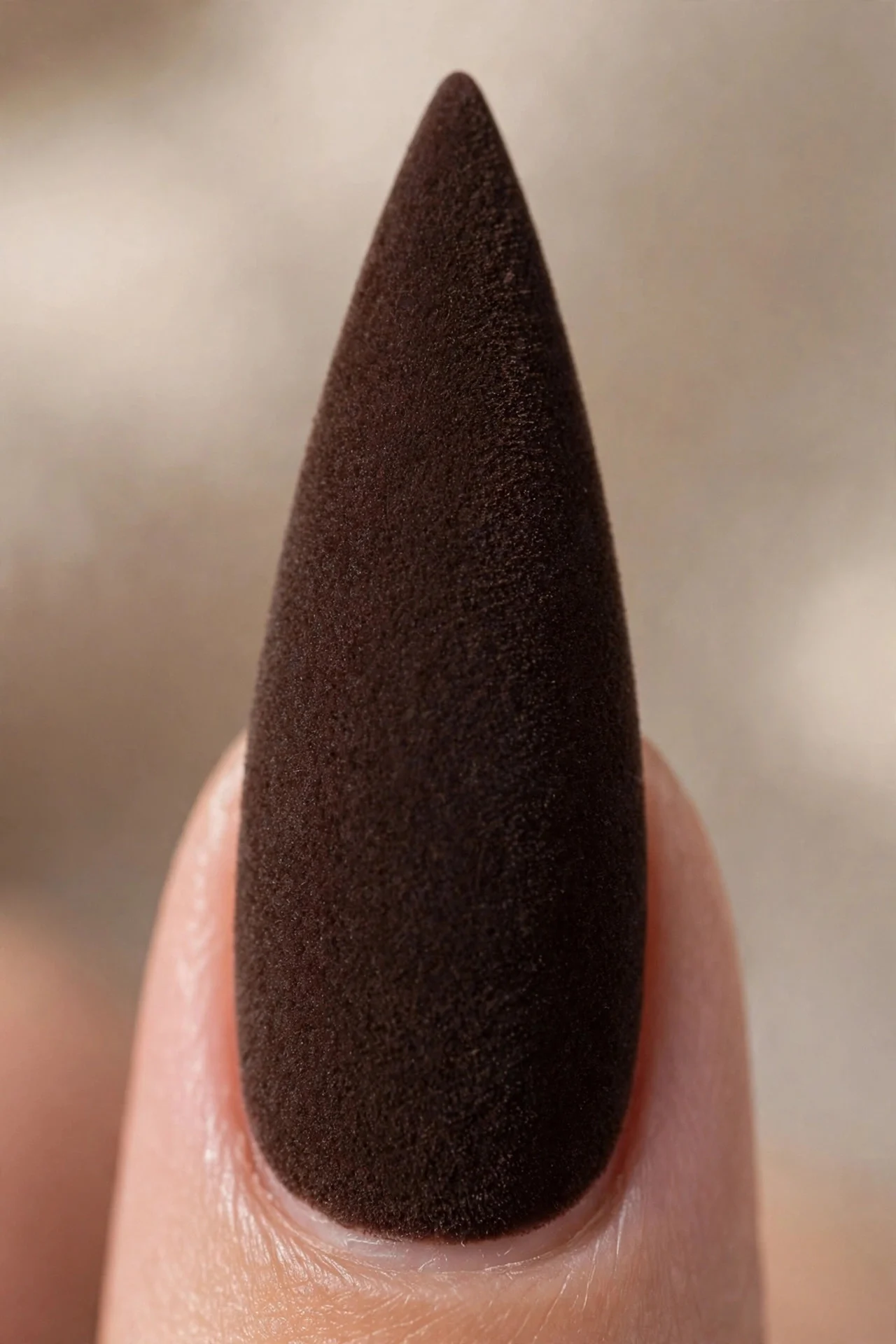 Macro of one stiletto fingernail in dark chocolate brown with a velvet matte finish, dramatic shape, soft light