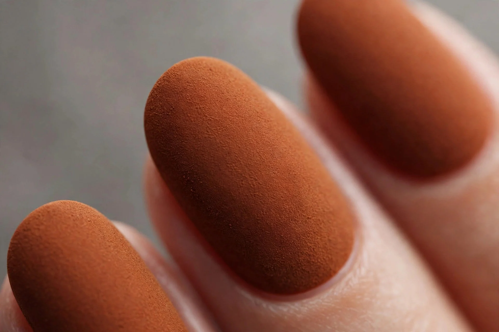 Oval nails in burnt cinnamon with matte top coat, suede-like finish, gray background