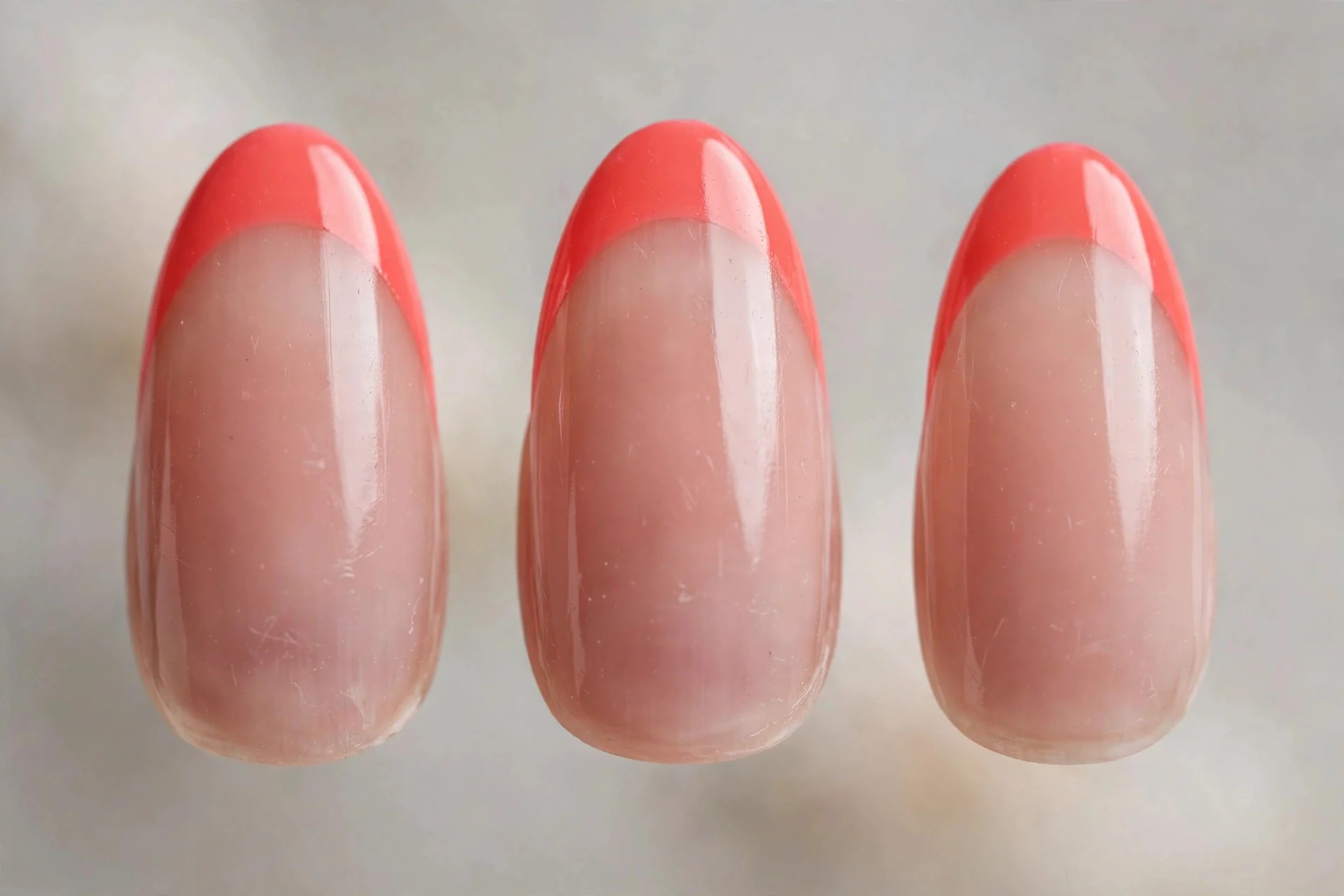 Sheer nude base with bright coral French tips, almond nails
