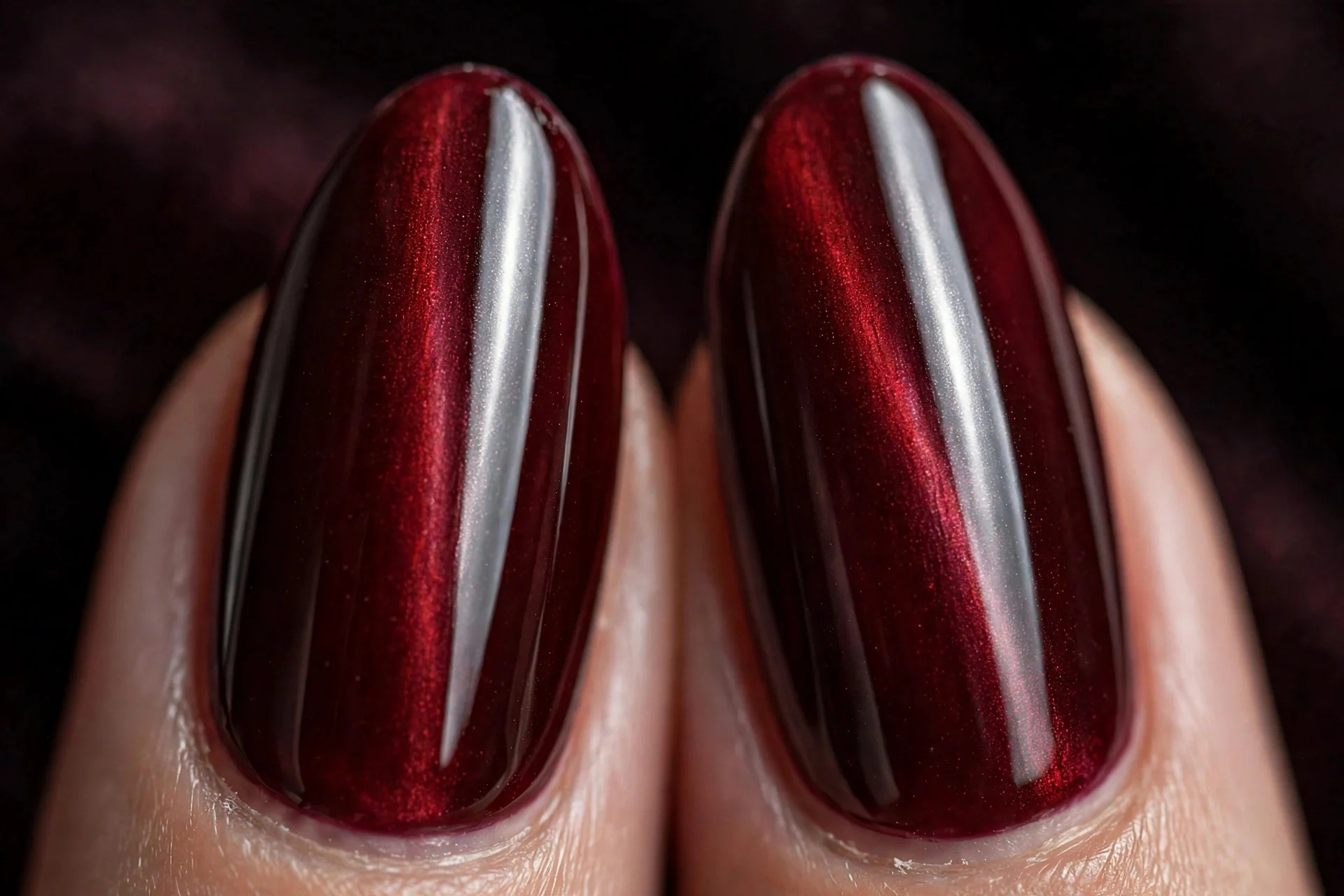 Extreme macro of two almond fingernails in oxblood cat-eye gel with a sharp vertical light band, rich glossy finish