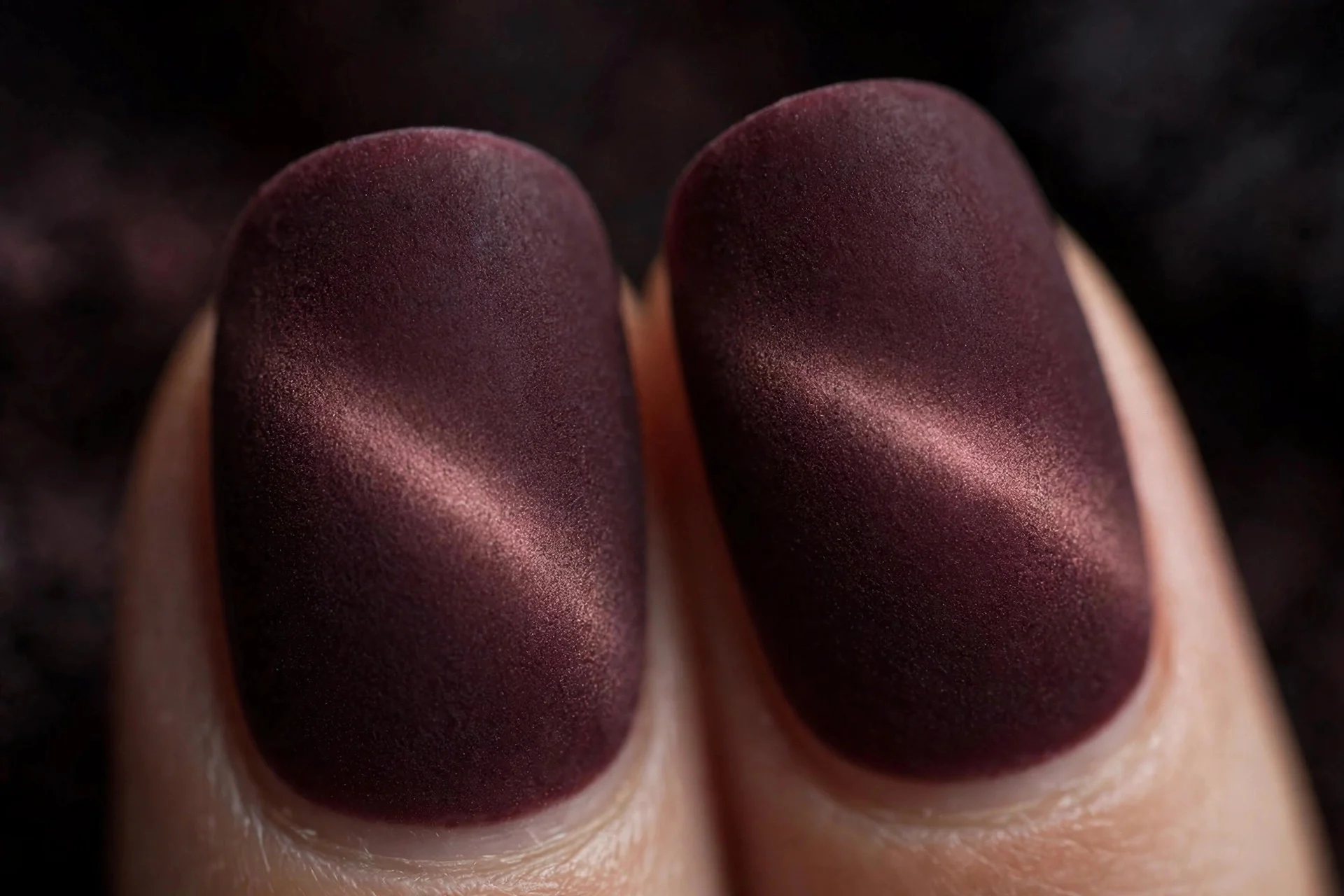 Extreme macro of two fingernails in merlot cat-eye gel with a diffused velvet band under matte top coat, soft textured finish