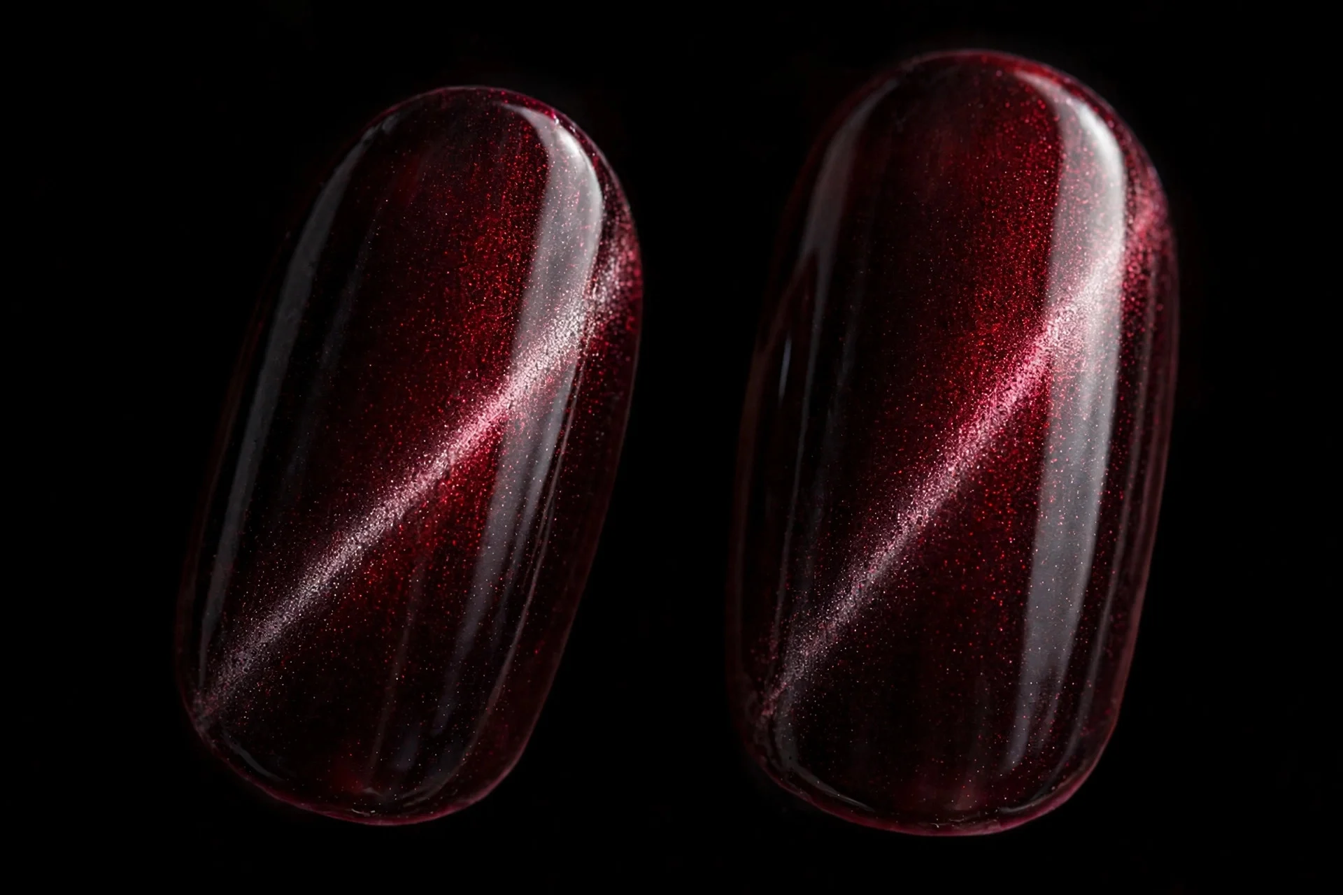 Extreme macro of two fingernails in blackened crimson cat-eye gel with the light band swept to one side, slimming effect