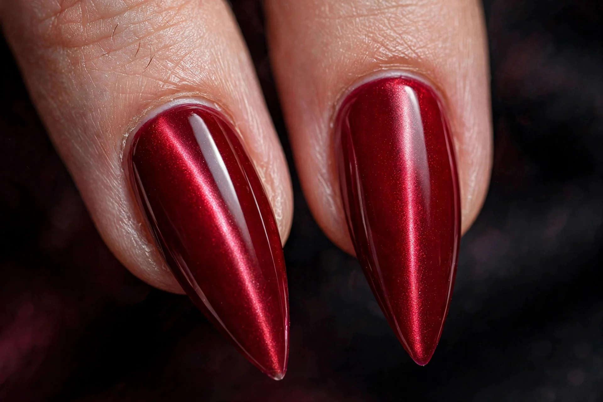 Extreme macro of two stiletto fingernails in crimson cat-eye gel with a sharp vertical band, dramatic pointed finish