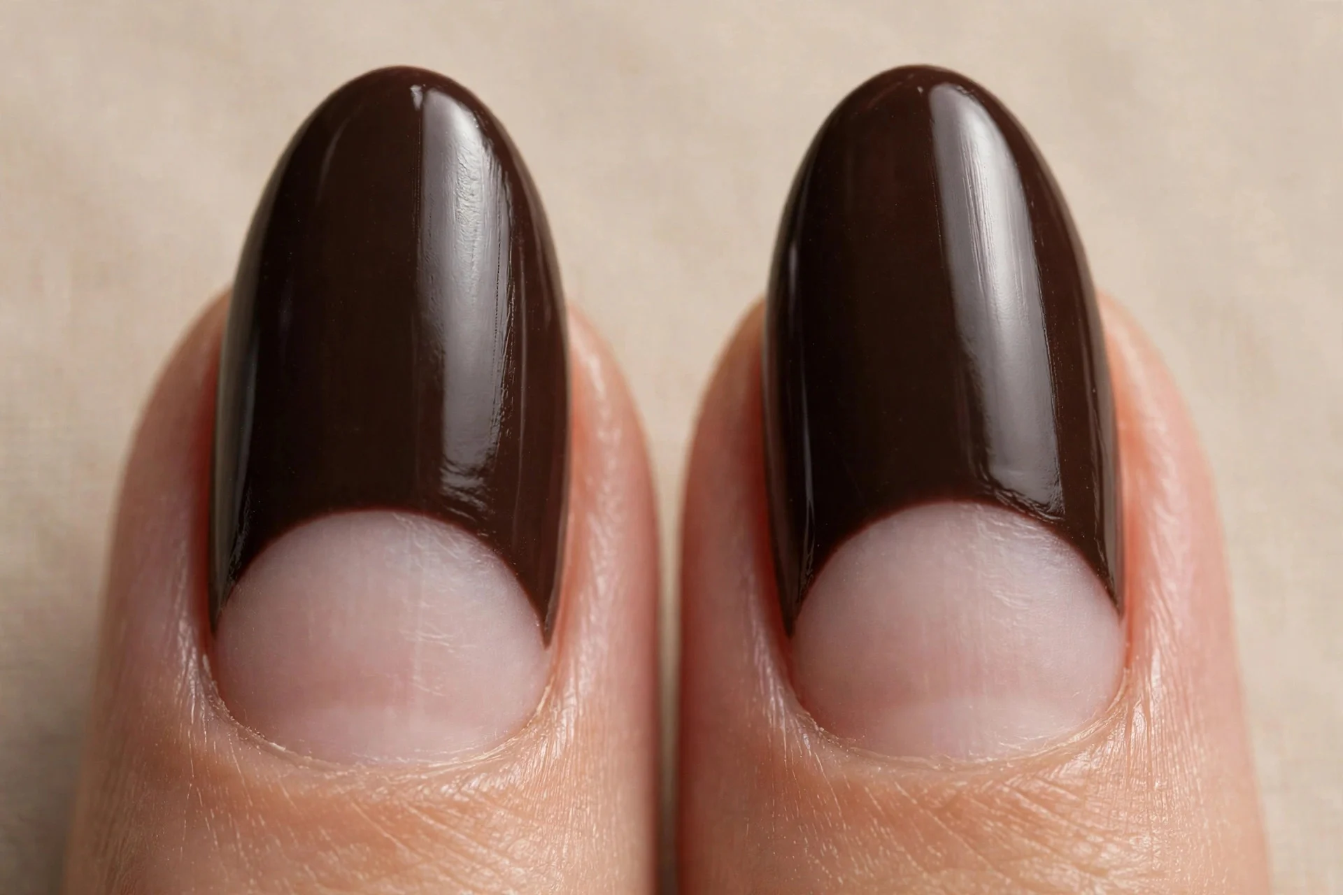 Almond nails in espresso with bare half-moon crescents at the cuticle, glossy, beige background