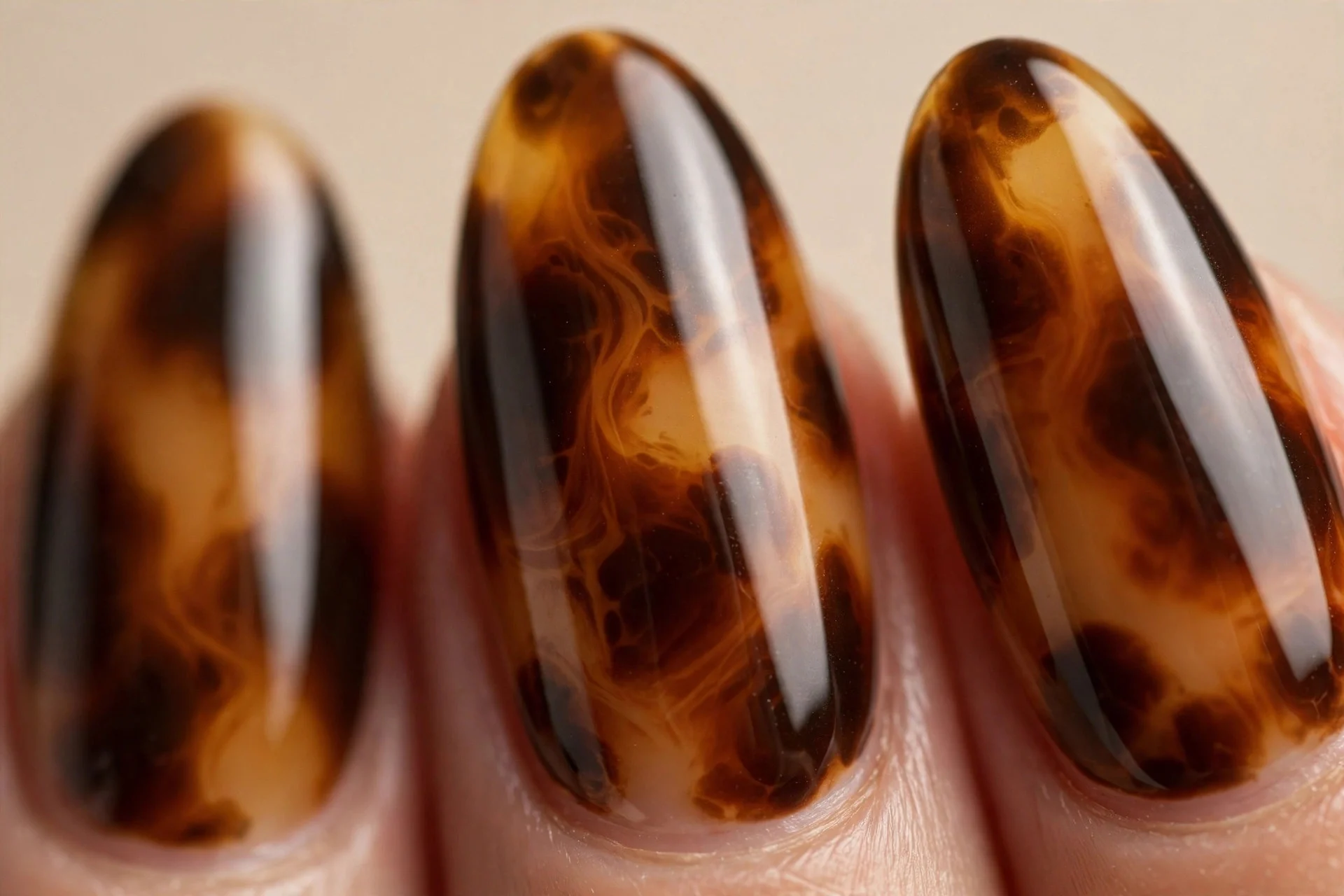 Almond nails with tortoiseshell pattern in espresso, amber and caramel, glossy, beige background