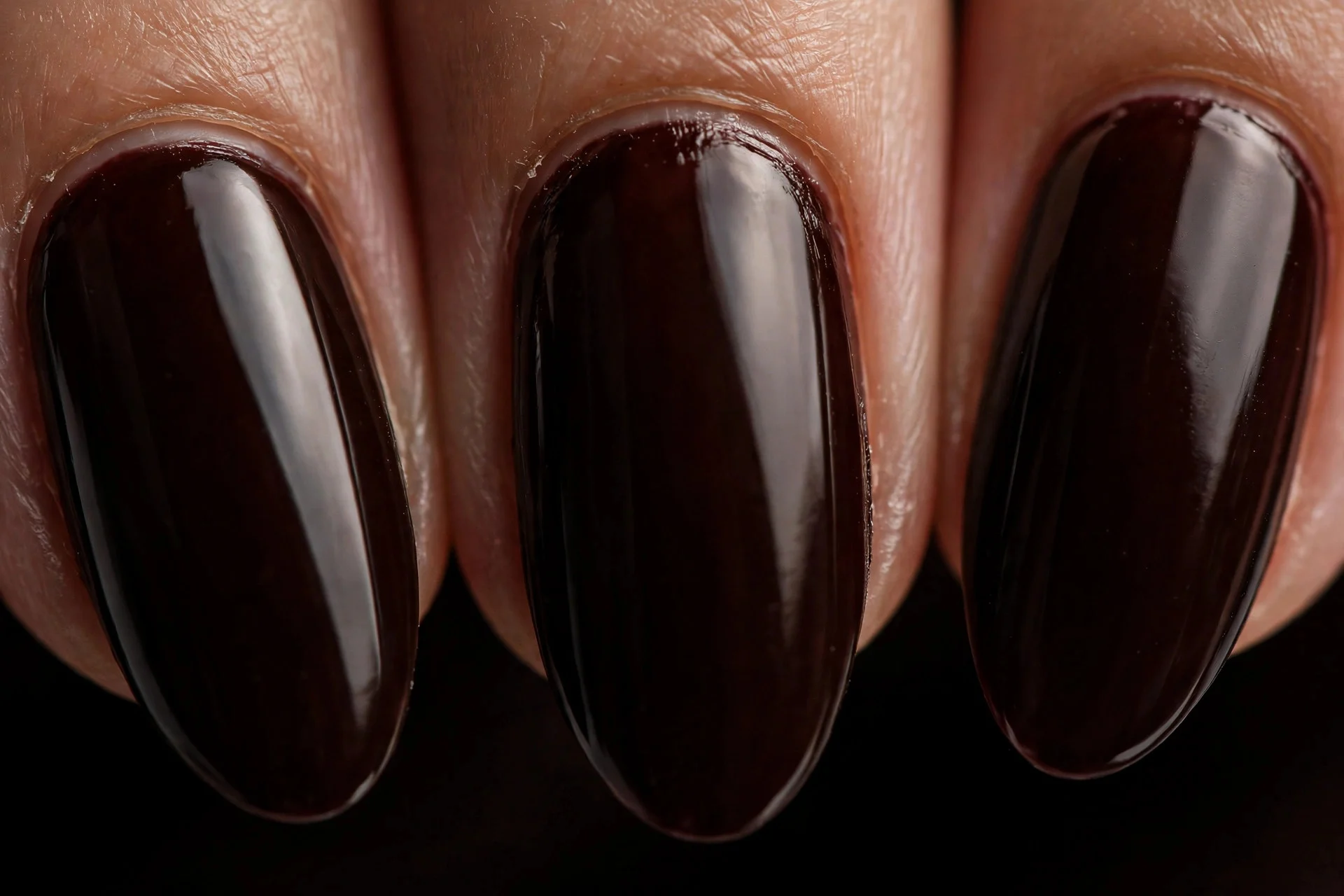 Almond nails in deep black-cherry brown polish, glossy, dark background