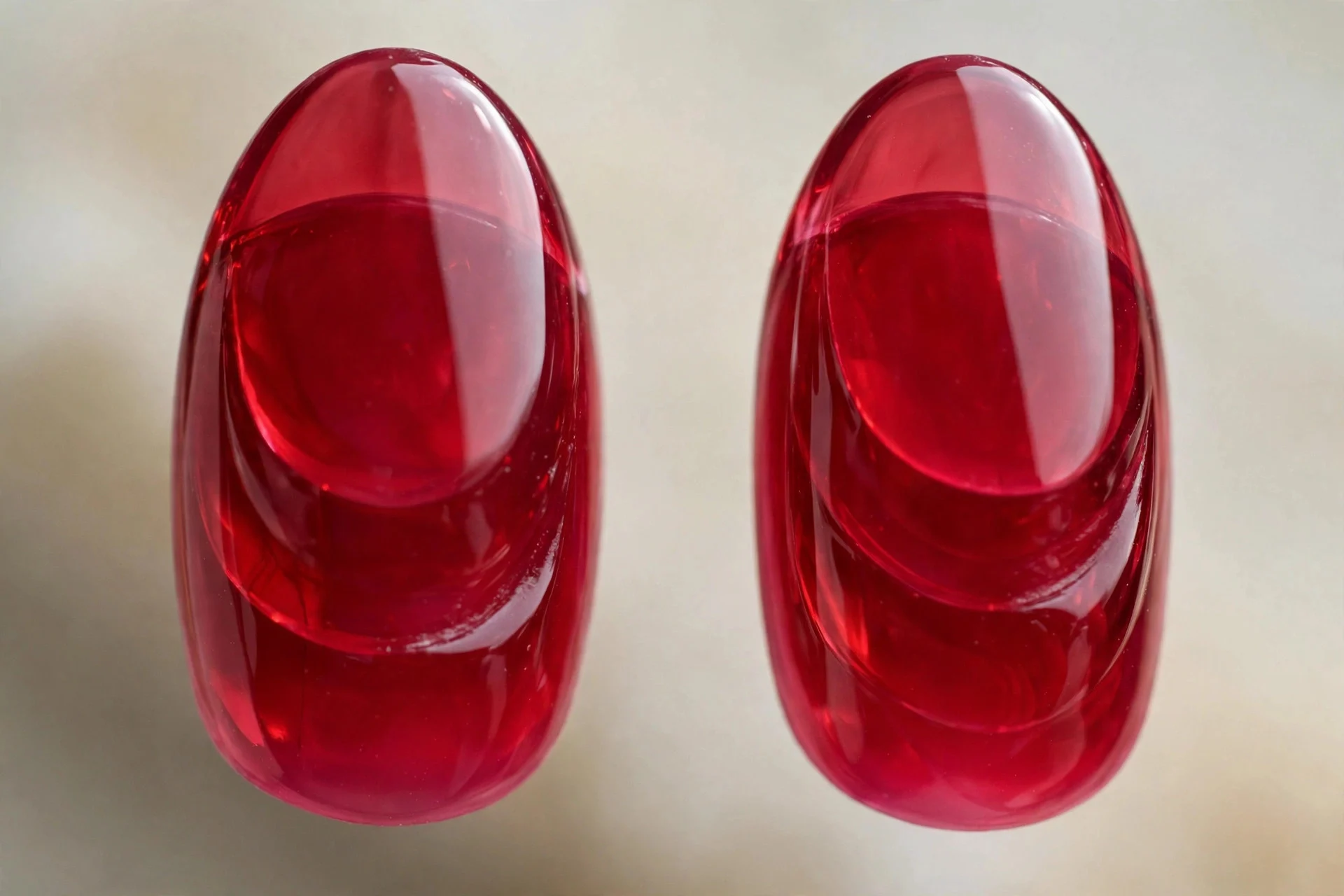 Extreme macro of two almond nails in deep raspberry-red tinted glass jelly with rich depth