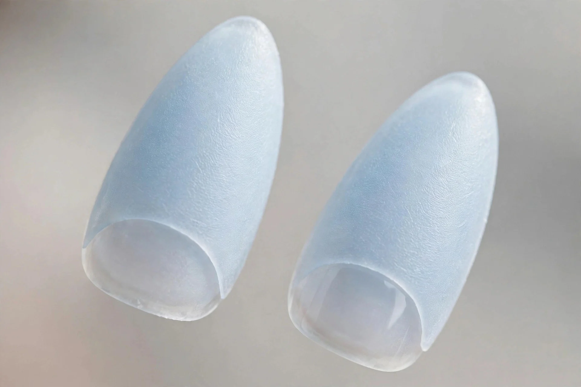 Extreme macro of two almond nails in pale ice-blue frosted glass with etched-ice matte finish