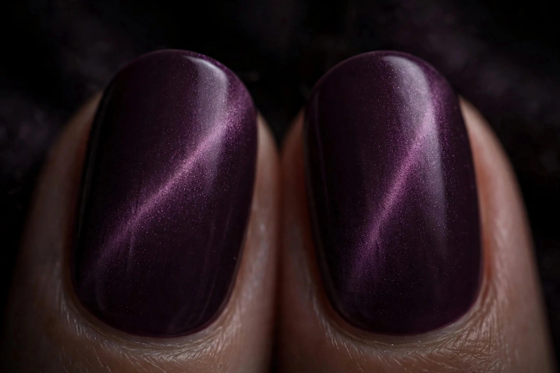 Extreme macro of two fingernails in deep plum cat-eye gel with a soft diffused velvet light band, dark moody background
