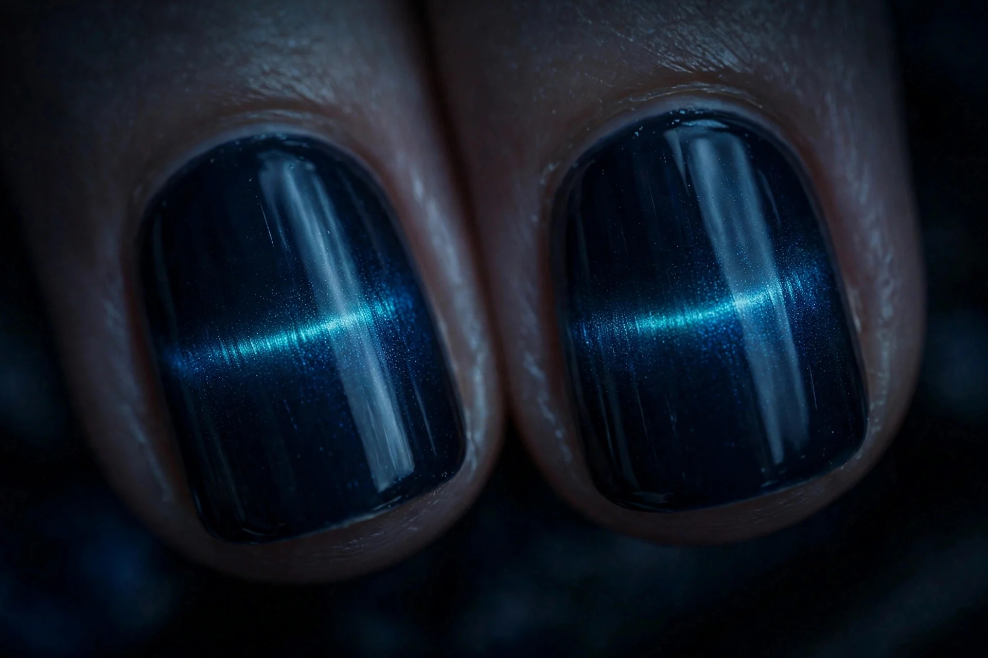 Extreme macro of two short fingernails in midnight blue cat-eye gel with a horizontal electric shimmer band, punk mood