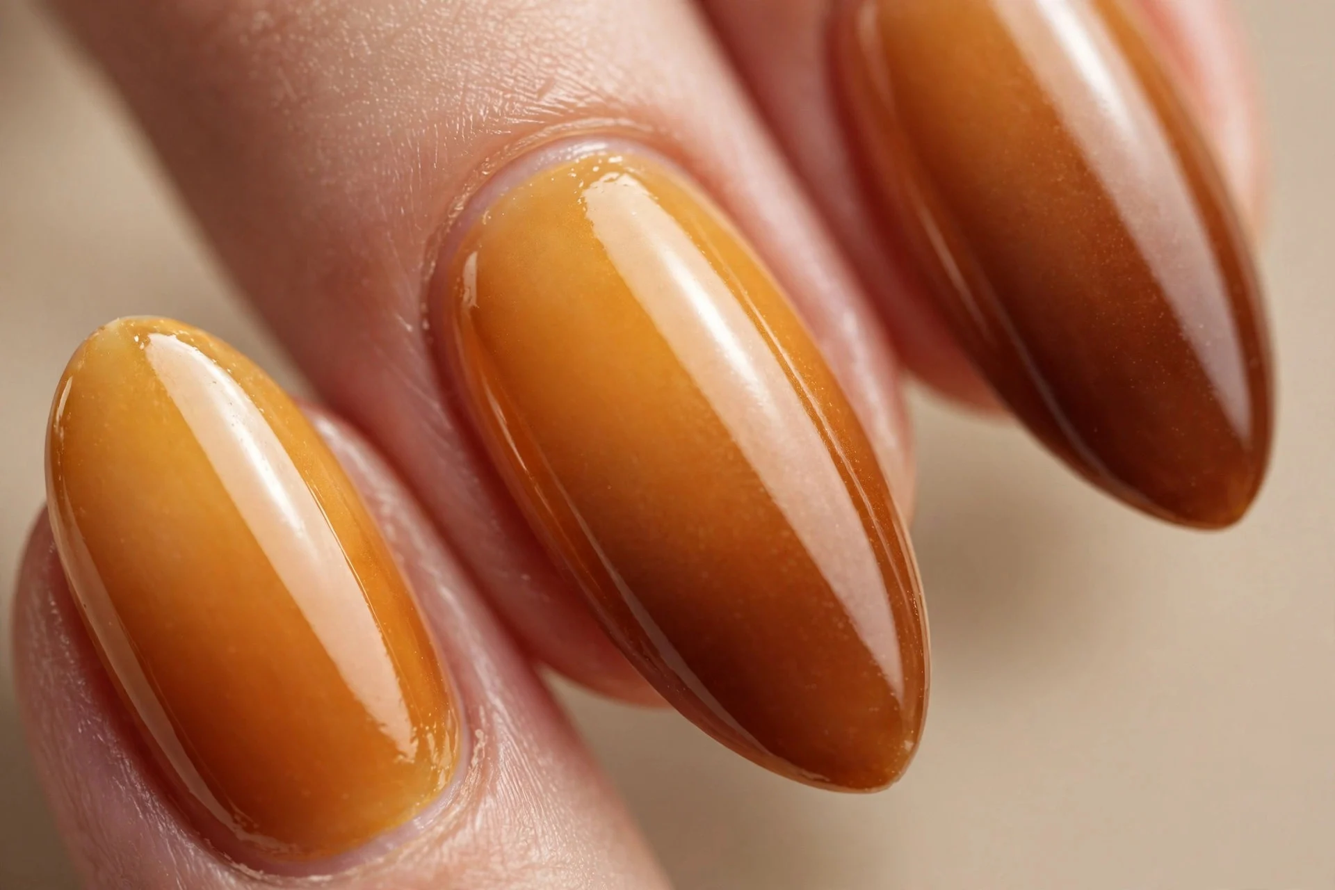 Almond nails with honey-to-caramel ombre fading from golden cuticle to deeper tip, glossy, beige background