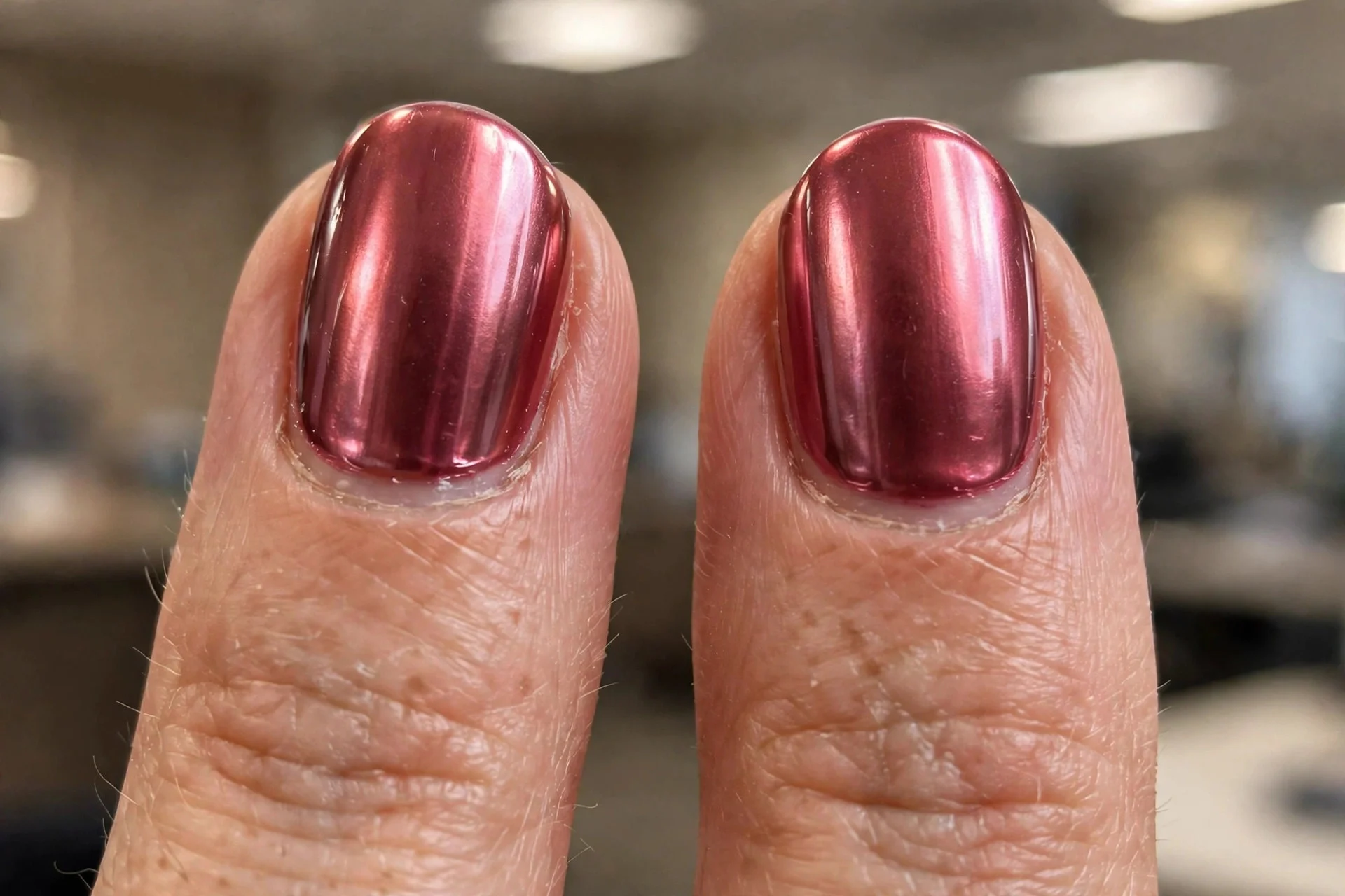 Extreme macro of two oval fingernails in deep rose chrome, rich polished pink with subtle reflectivity, office lighting