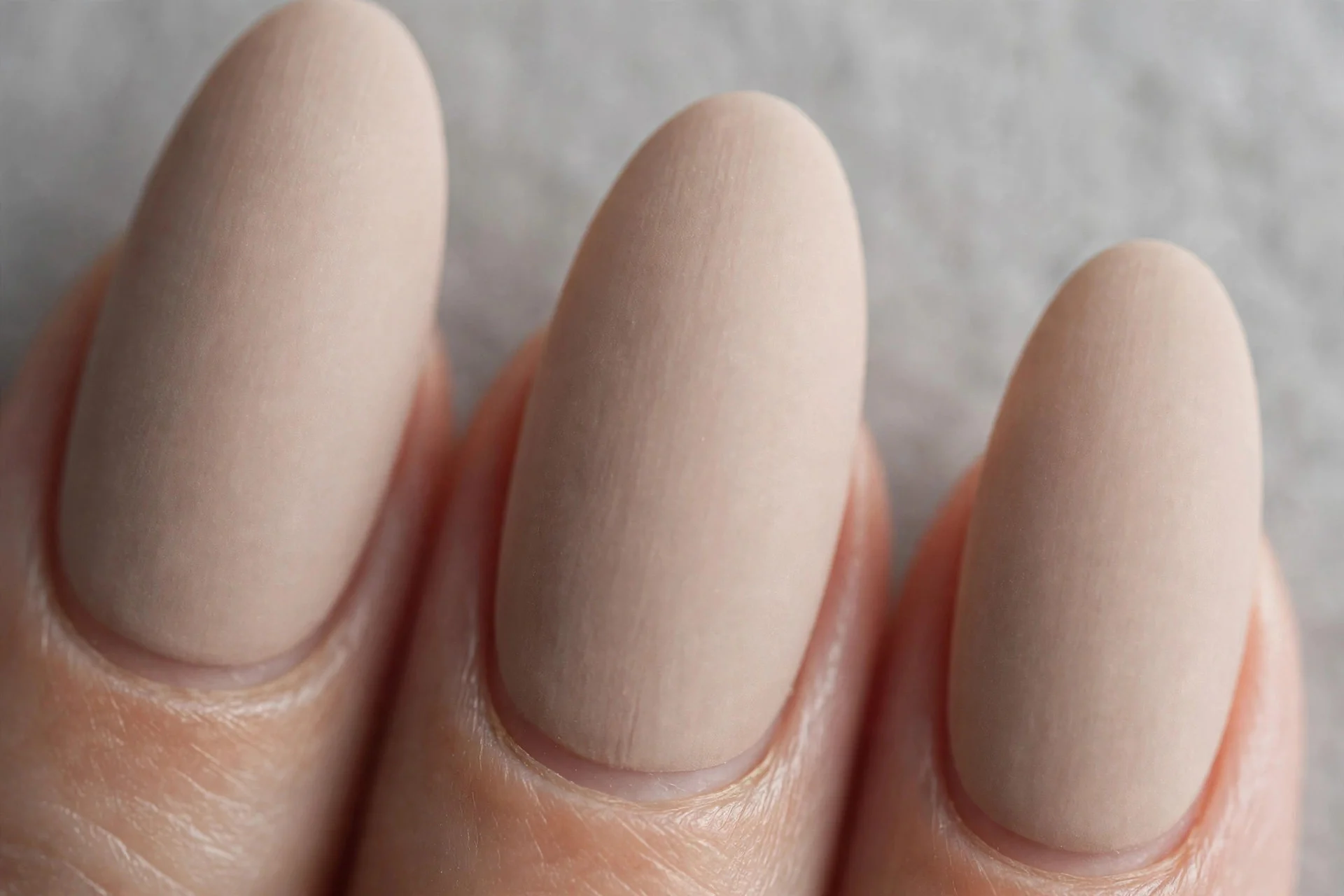Almond nails in matte beige-nude polish, soft grey background