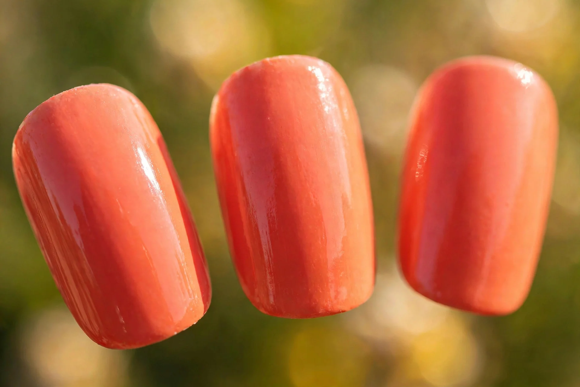 Warm sunset coral polish, short almond nails in bright sunlight