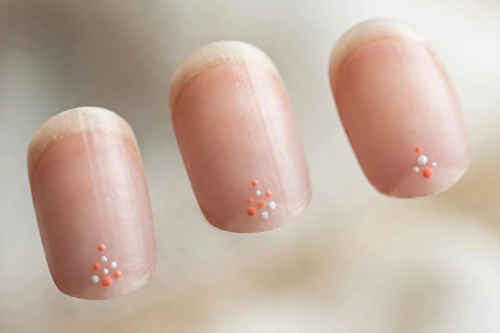 Bare nails with small coral and white dots near cuticles, oval