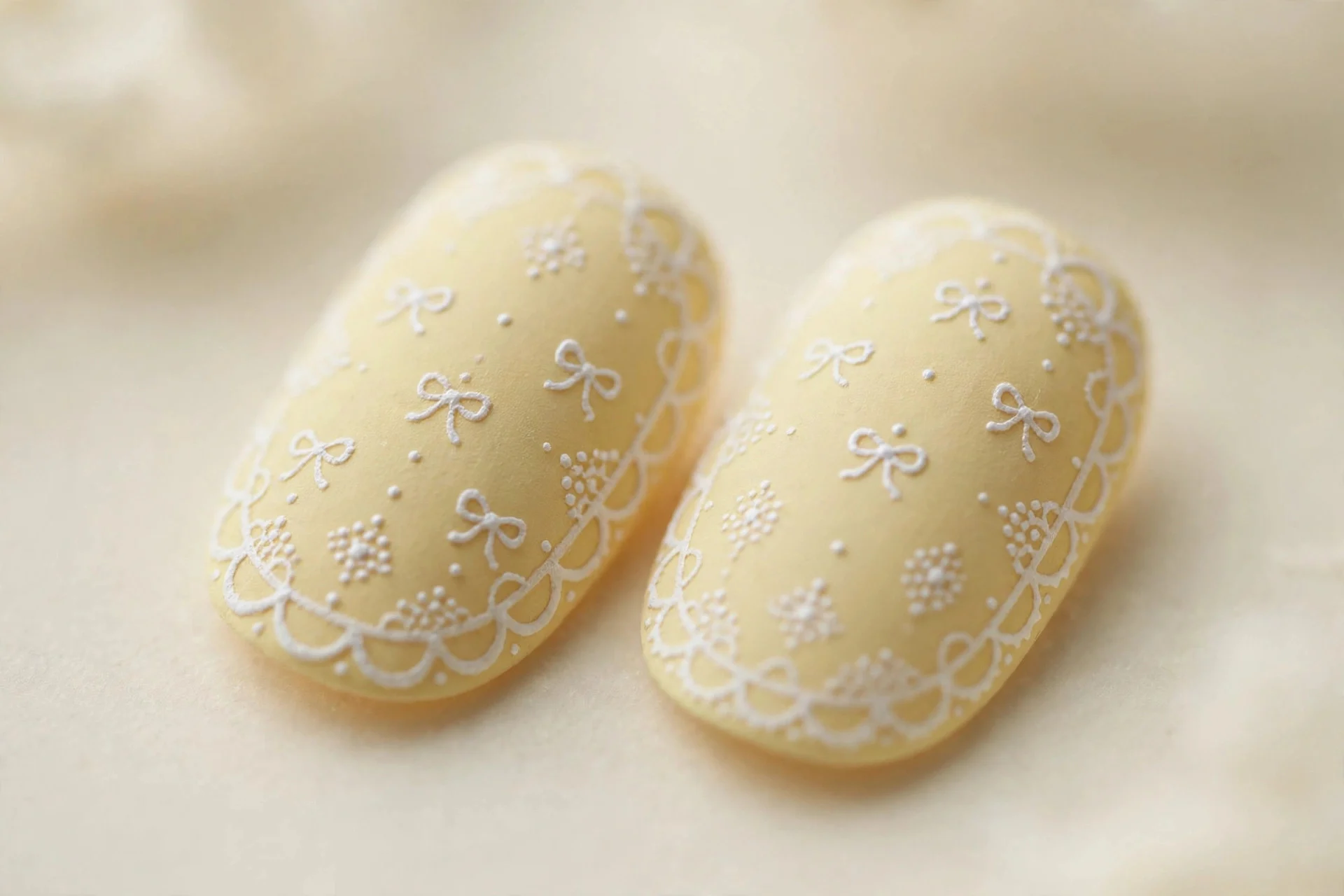 Oval nails with hand-painted white lace dots and scallops over butter yellow, matte, cream background