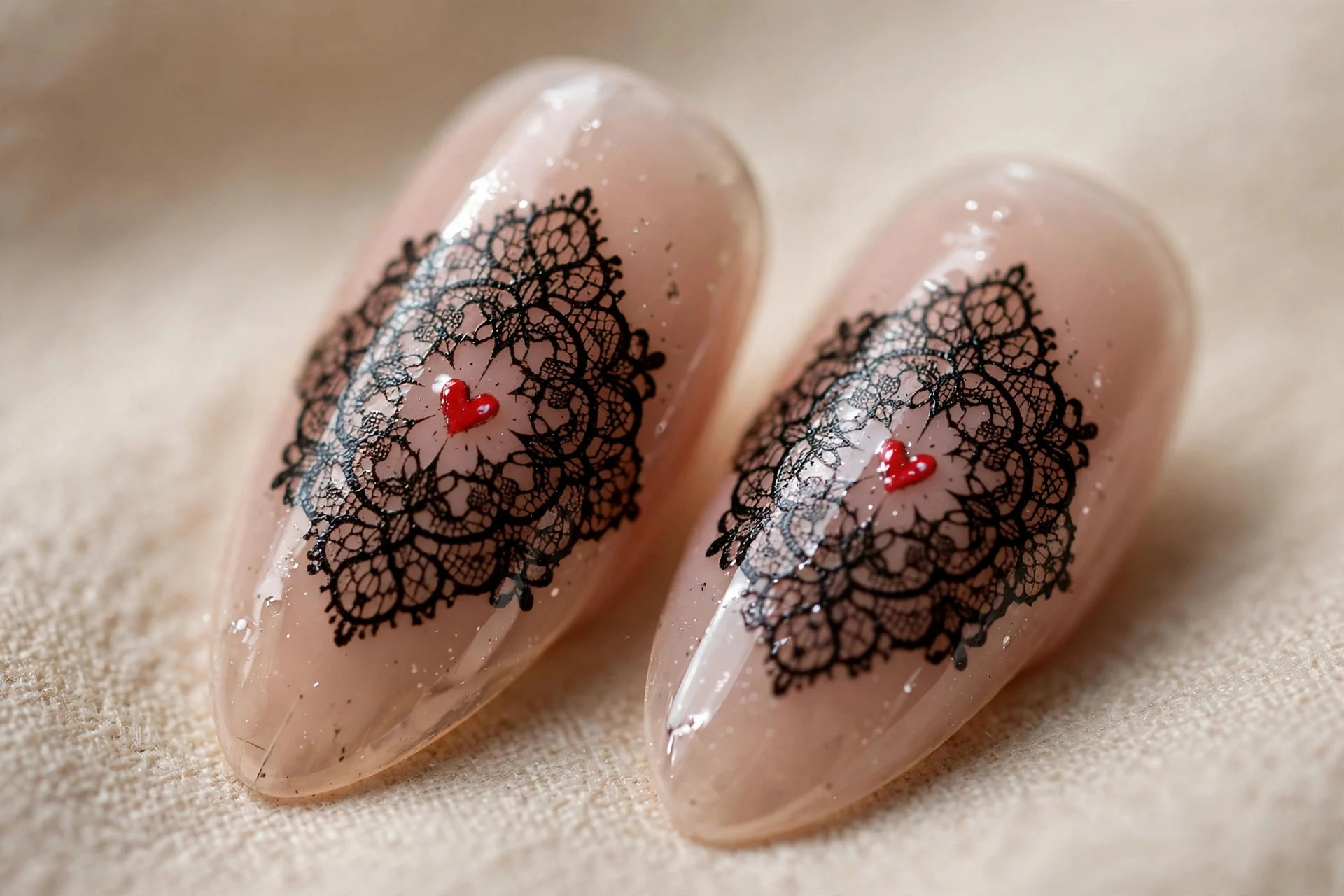 Almond nails with black lace stamping over sheer nude, tiny red heart at each medallion center, glossy, beige background