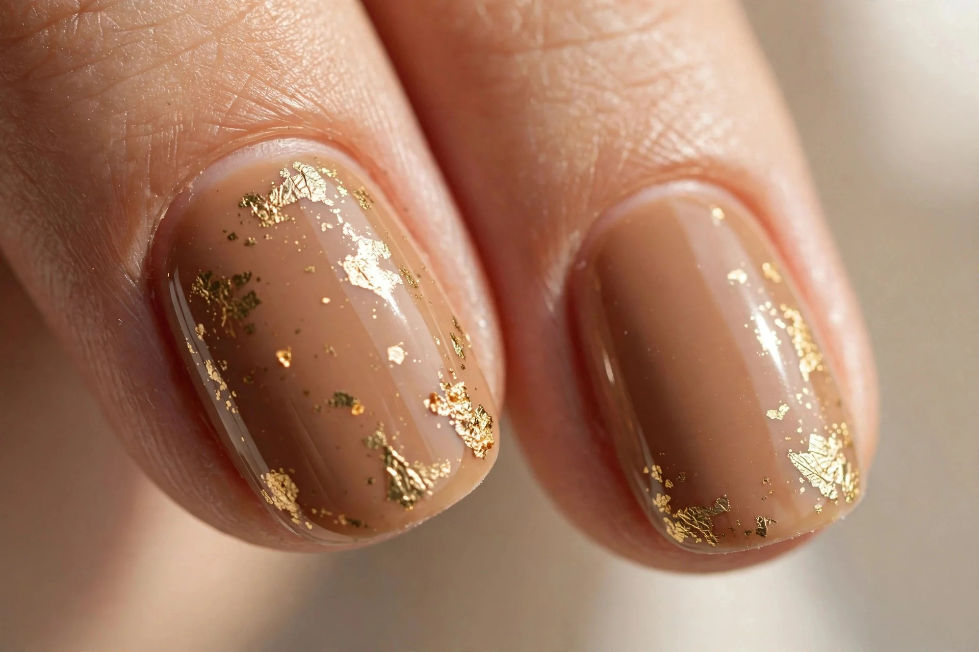 Latte-brown nails with delicate gold foil flakes as accents.