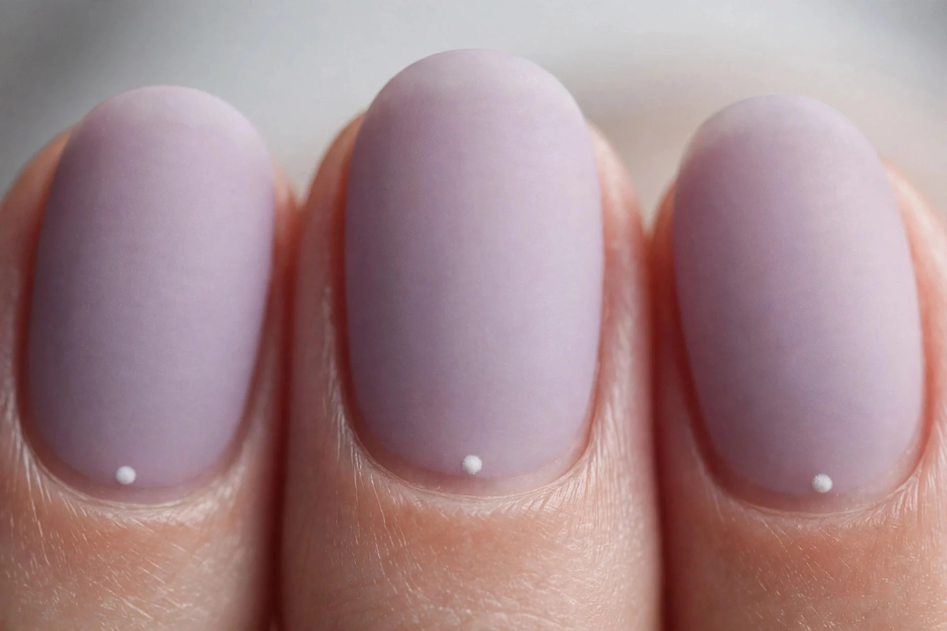 Matte sheer lavender nails with tiny white dot at cuticle, short oval