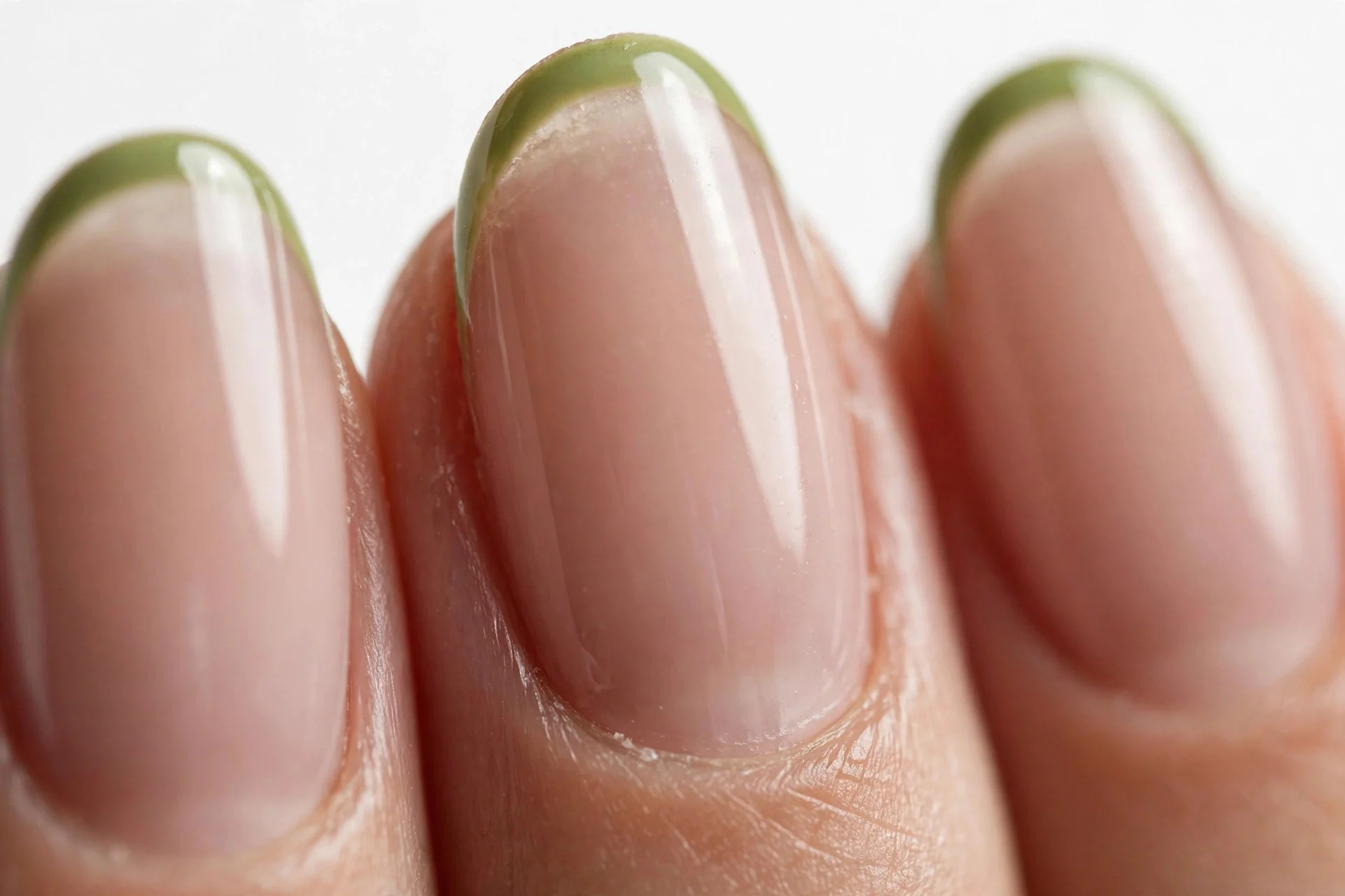 Almond French nails with thin matcha green tips over sheer nude, glossy, white background