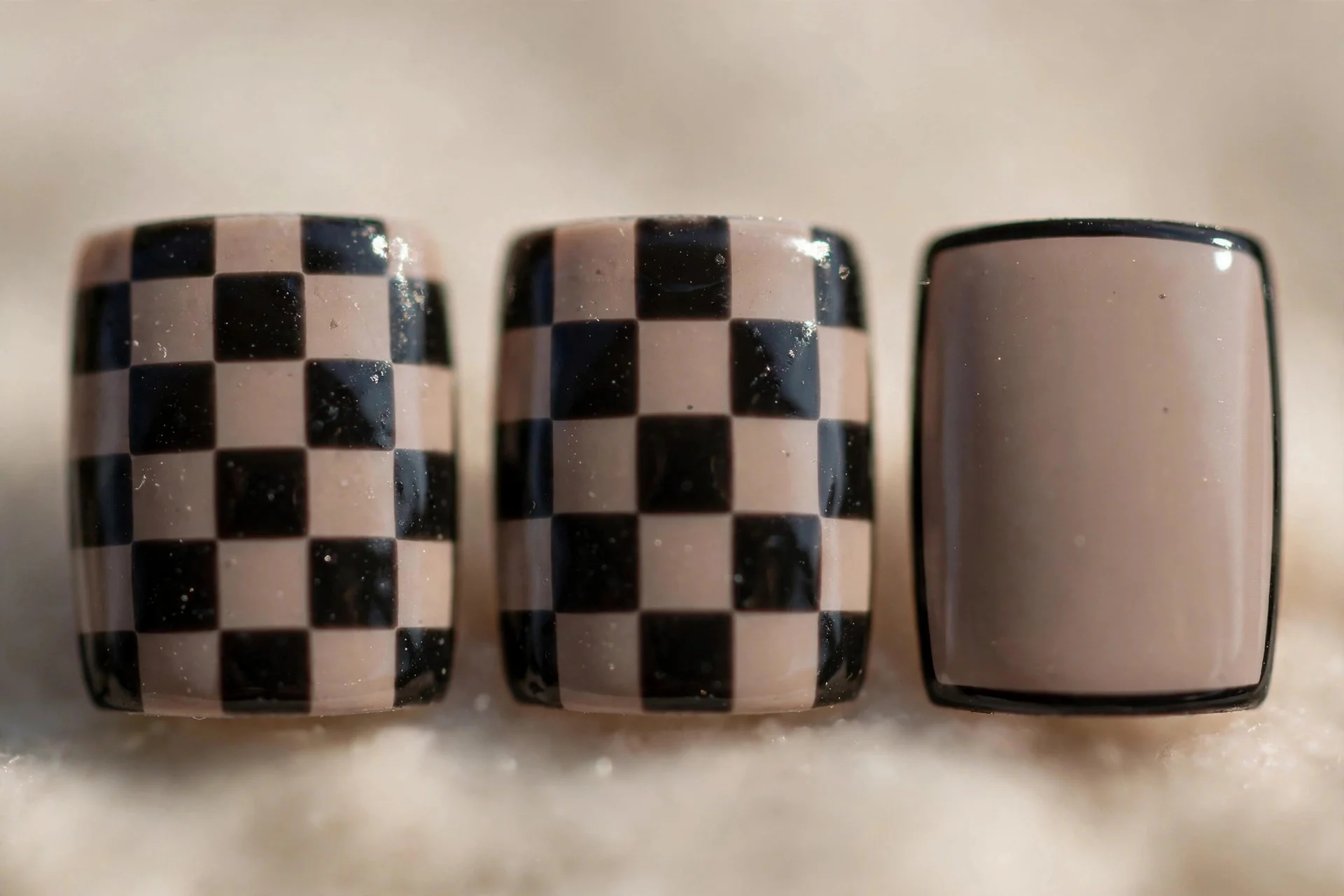Extreme macro of three square nails in taupe and black checkerboard alternating with plain taupe, glossy