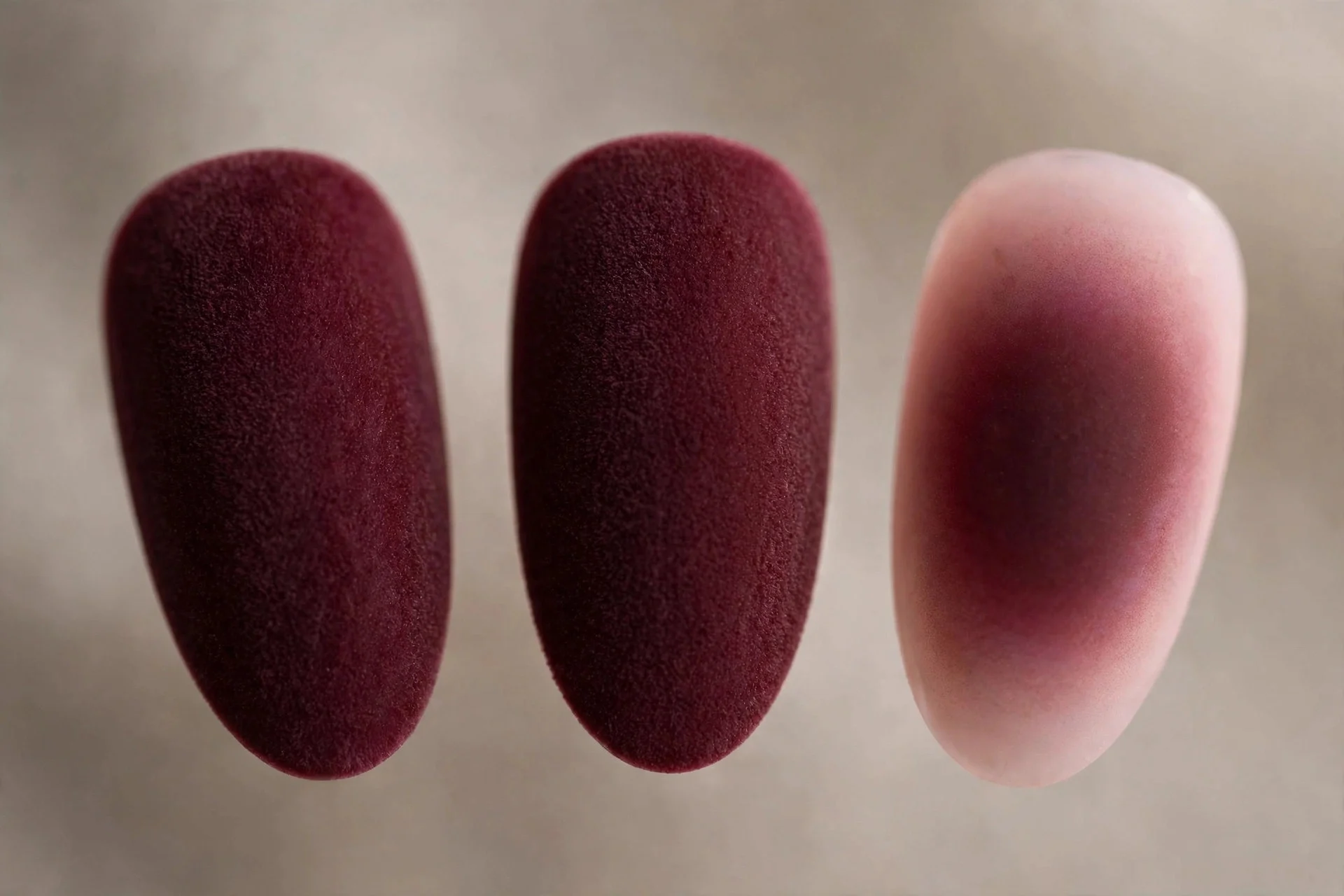 Extreme macro of three nails in matte burgundy velvet with one burgundy-to-blush aura nail, neutral background