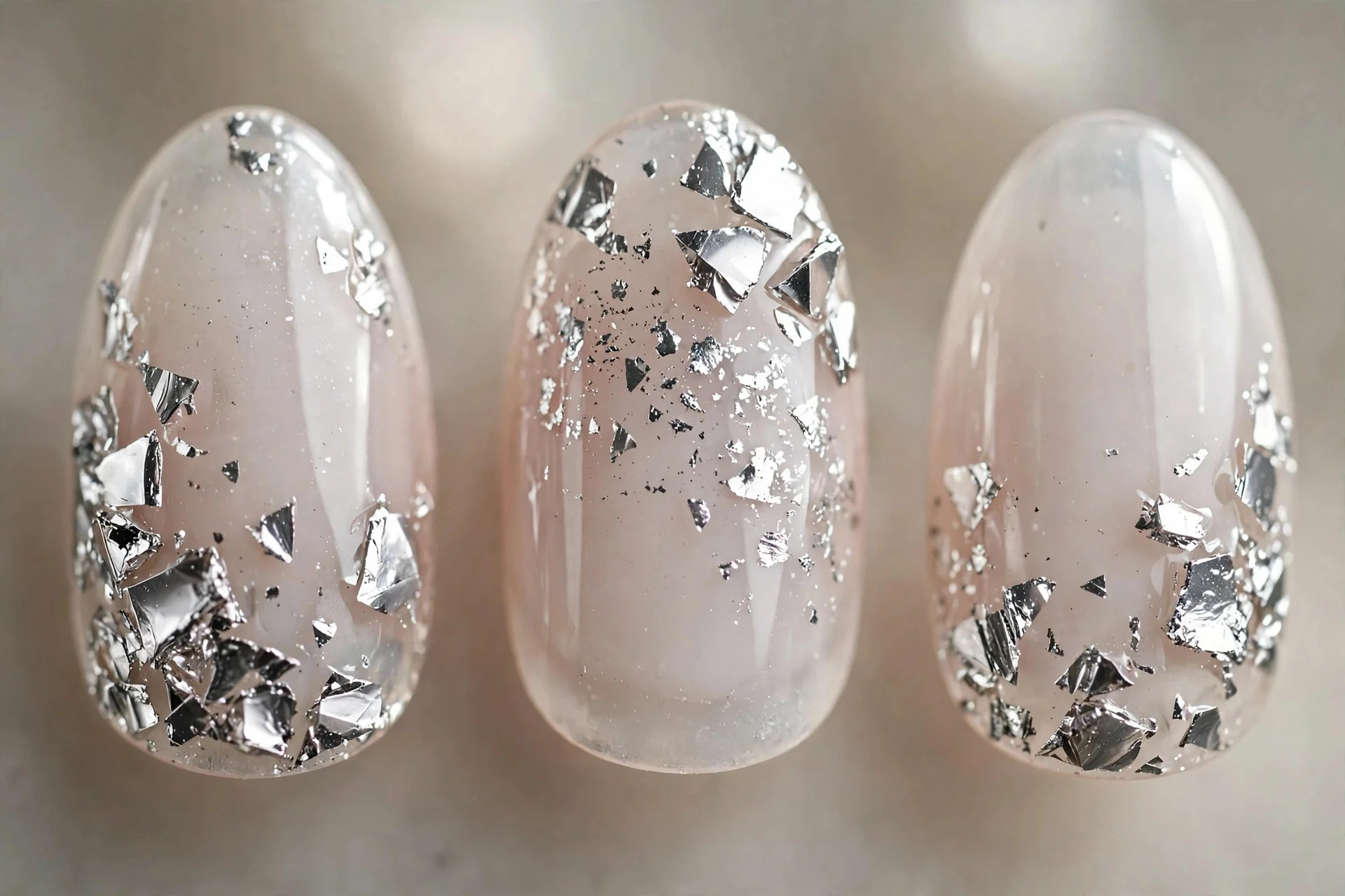 Extreme macro of three almond nails with milky base and scattered silver chrome fragments, glossy
