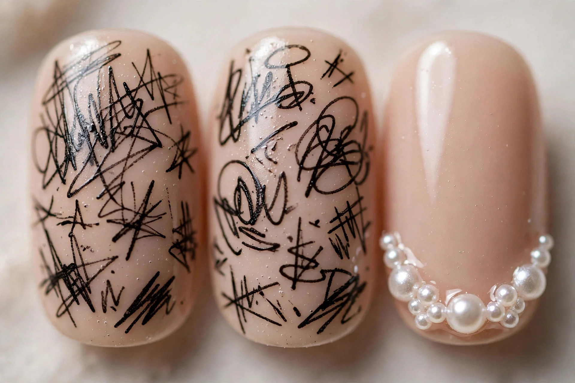 Extreme macro of three nude nails with black graffiti scribbles and small pearl clusters, neutral background