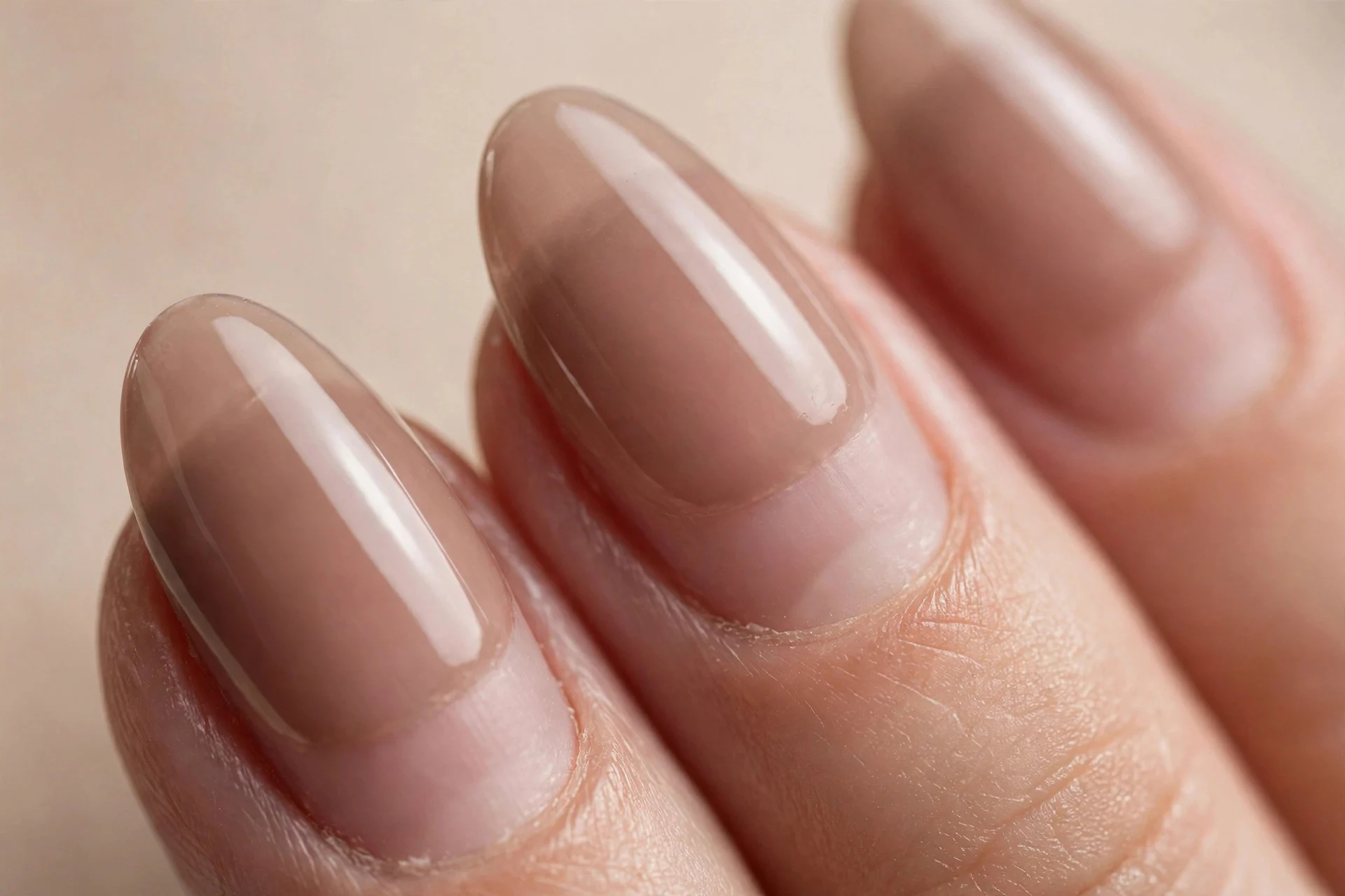 Almond nails with a sheer washed mocha tint, visible natural nail, glossy, beige background