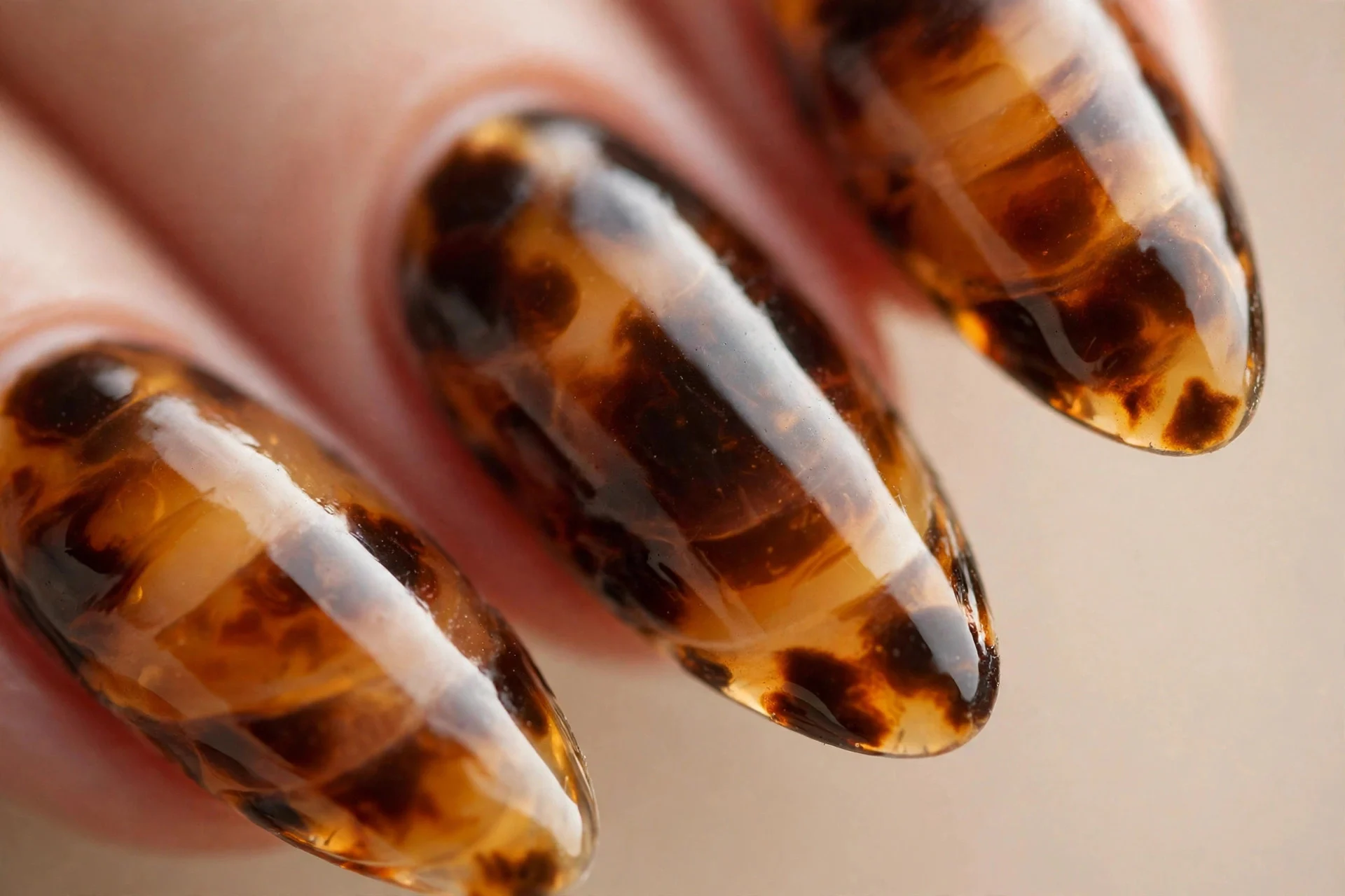 Almond nails with tortoiseshell pattern in amber, caramel and dark brown jelly layers, glossy, beige background