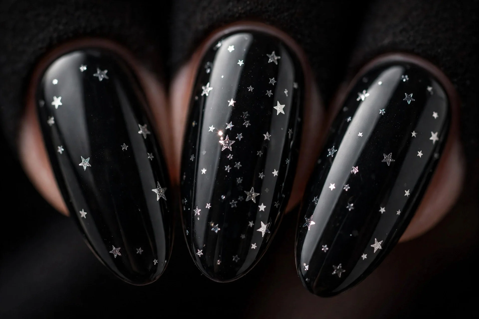 Almond nails in black gel with tiny silver star decals, dark background