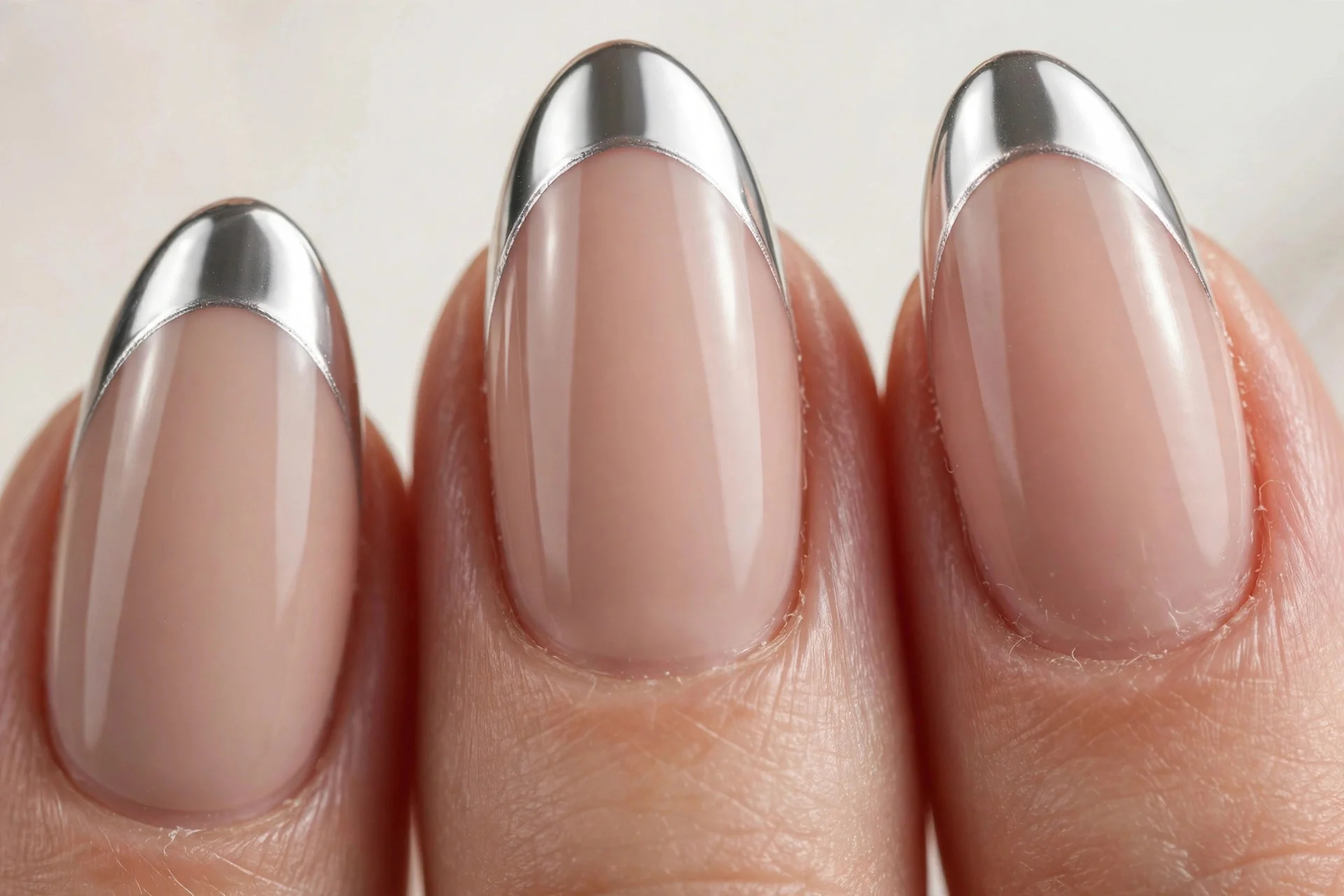 Almond nails with nude base and silver mirror chrome French tips, pale background