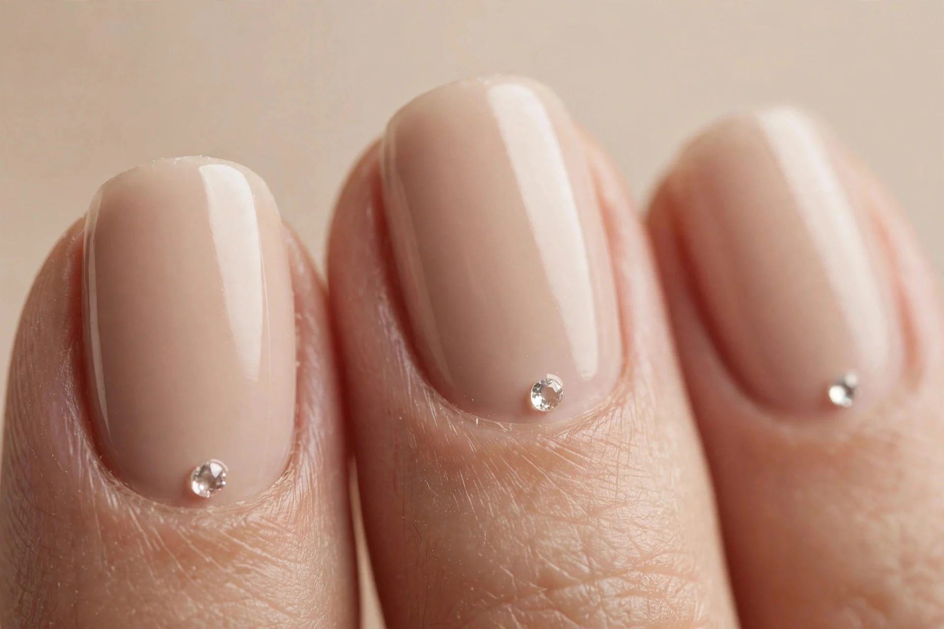 Nude nails with tiny crystal at each cuticle, soft beige background