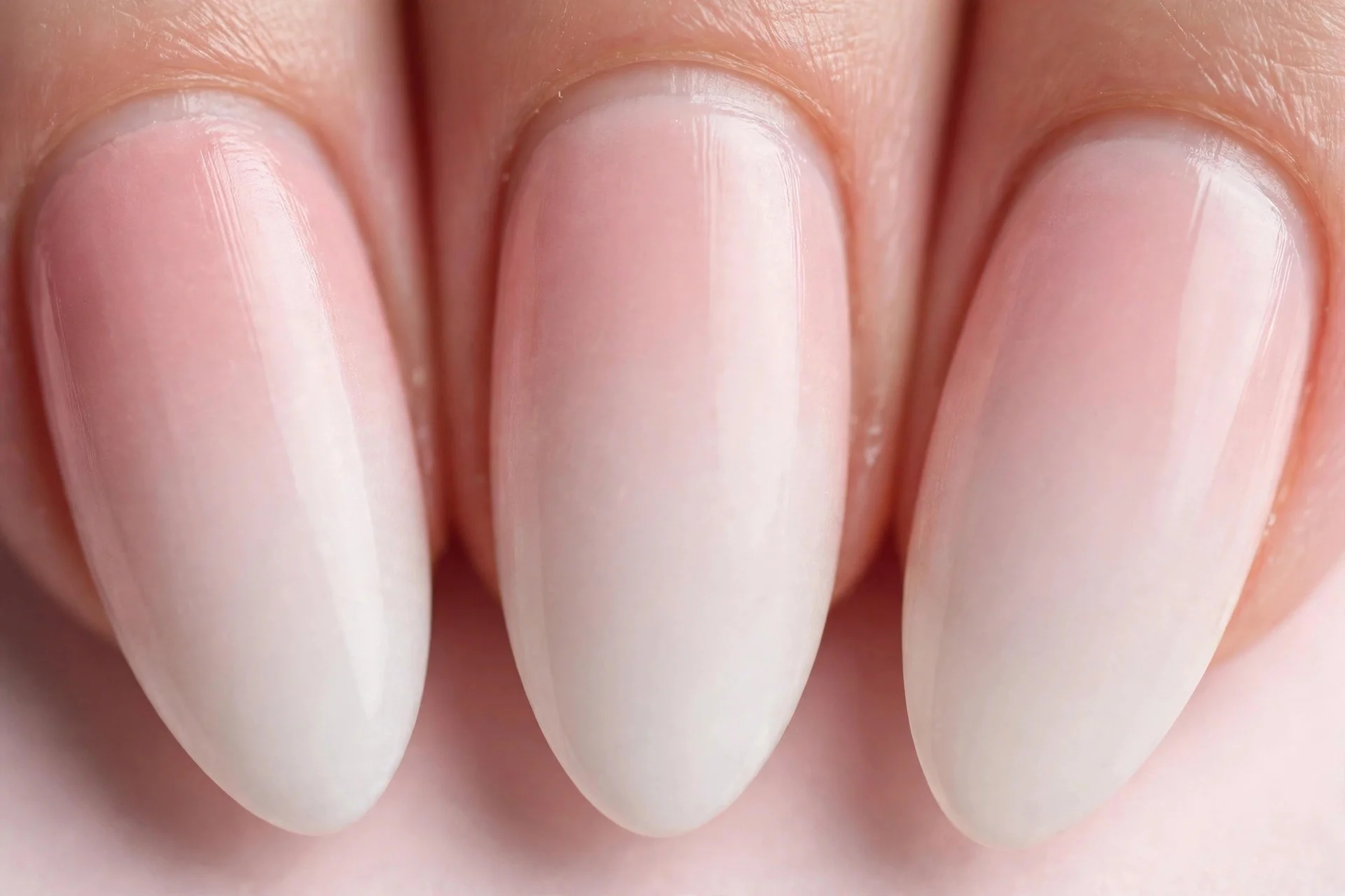 Almond nails with blush pink to milky white ombr&eacute;, pale pink background