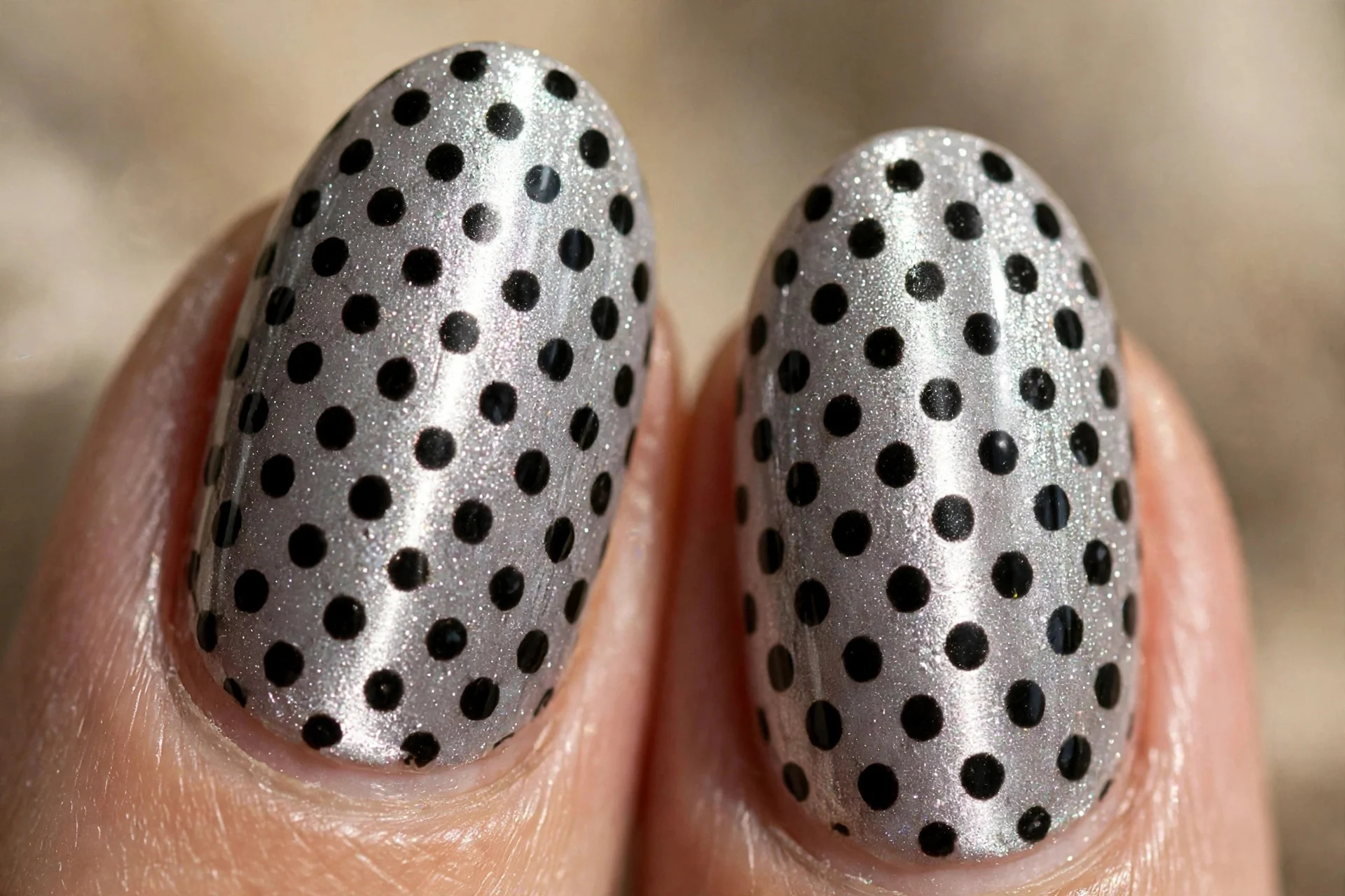Extreme macro of two oval fingernails in silver cat-eye gel with a sharp vertical light band, hand-painted black polka dots i