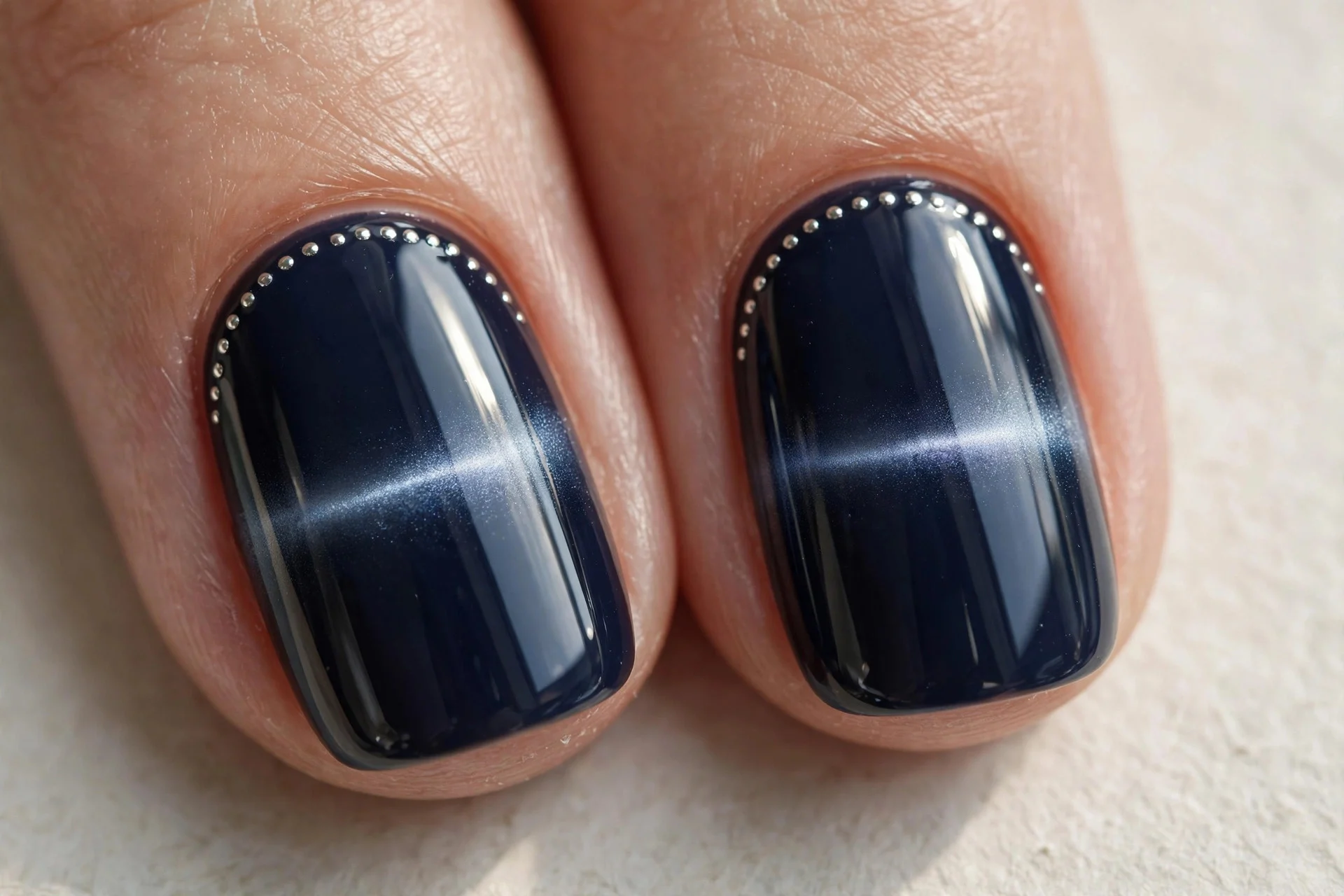 Extreme macro of two fingernails in midnight navy cat-eye gel with a horizontal shimmer band, small silver dots arcing along