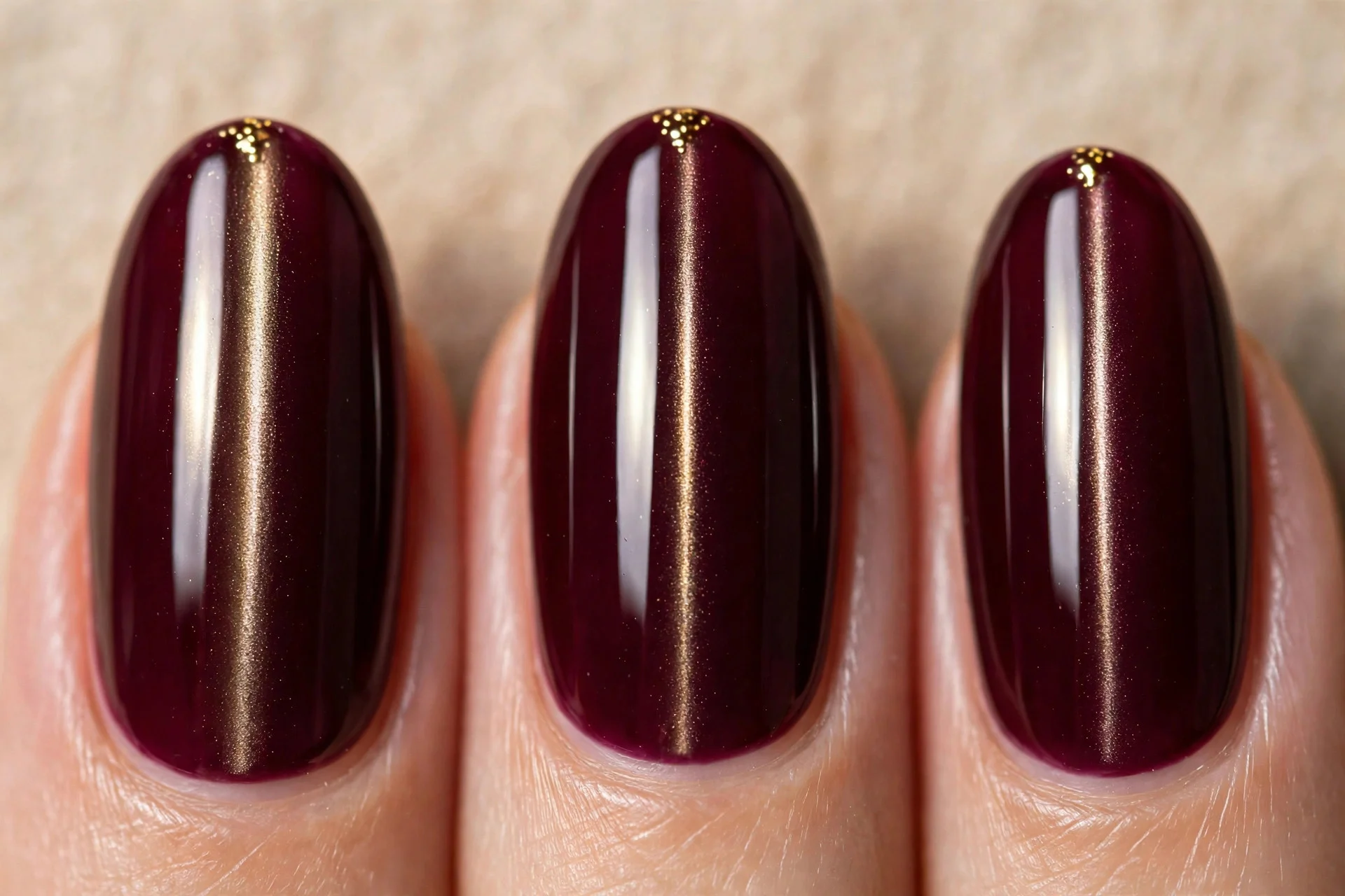 Extreme macro of three fingernails in wine-burgundy cat-eye gel with a vertical light band, tiny gold dots clustered near the