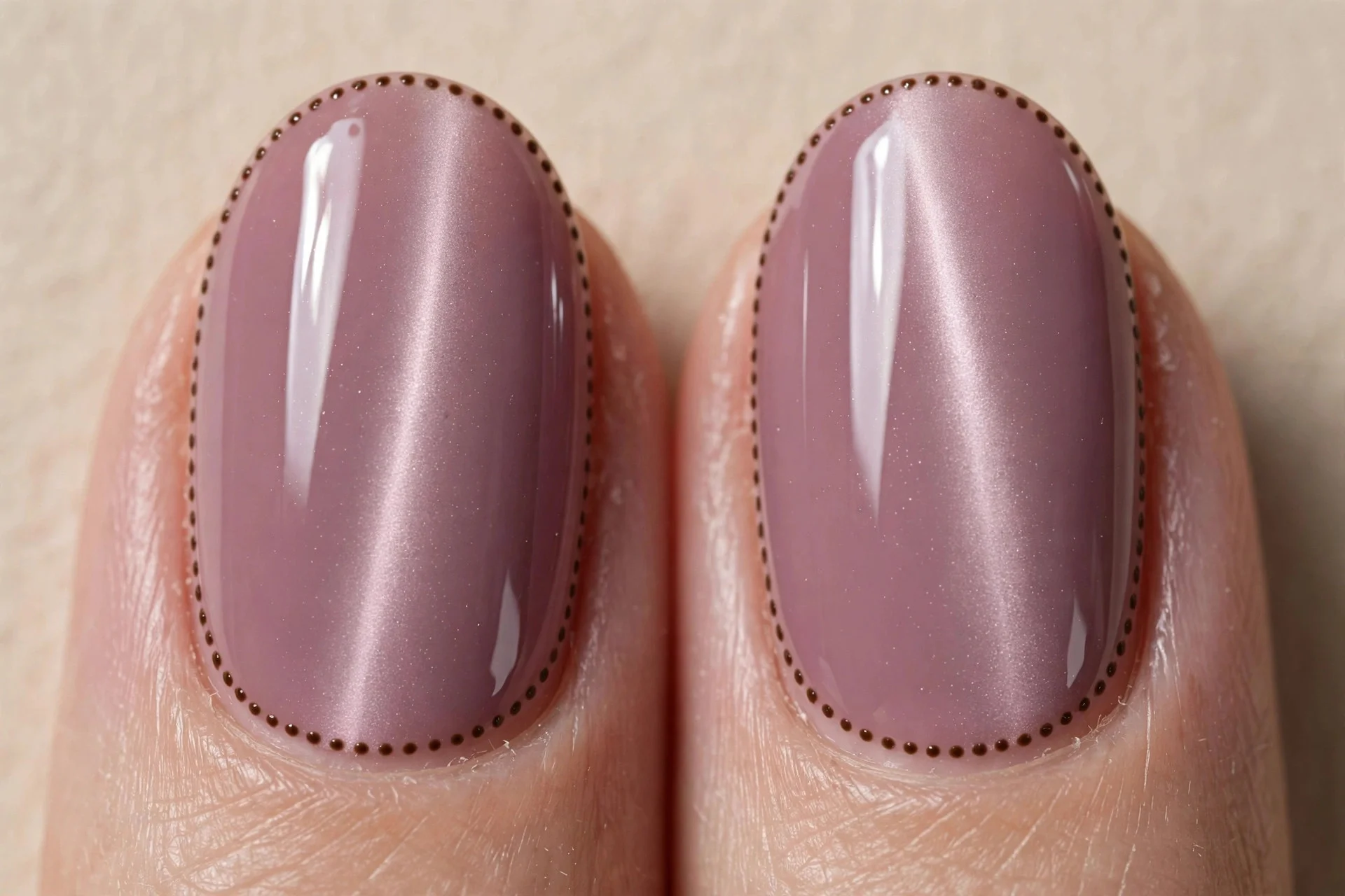 Extreme macro of two oval fingernails in soft mauve cat-eye gel with a gentle light band, small espresso dots forming a borde