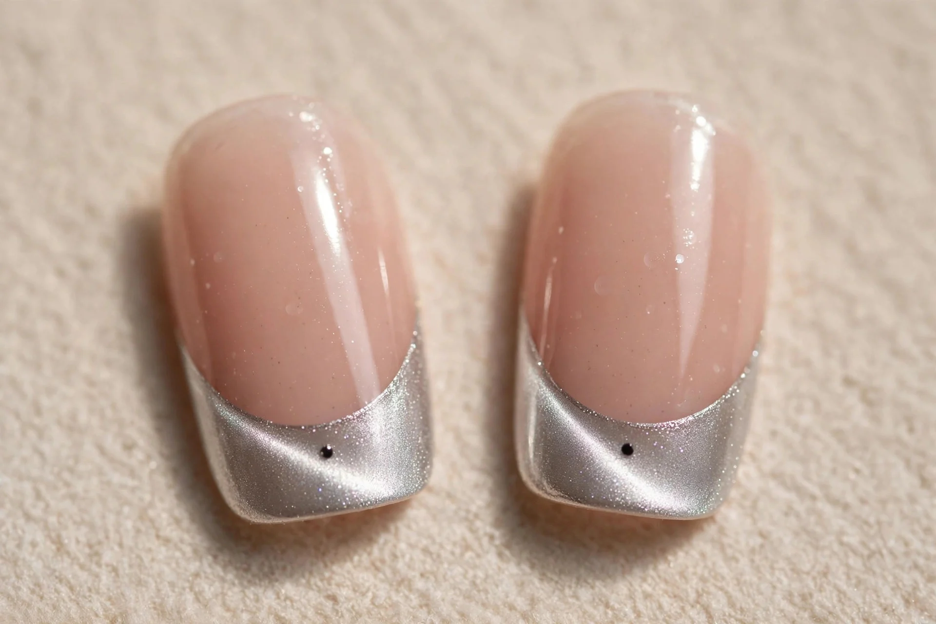 Extreme macro of two fingernails with nude bases and silver cat-eye French tips showing a shimmer line, one small black dot c