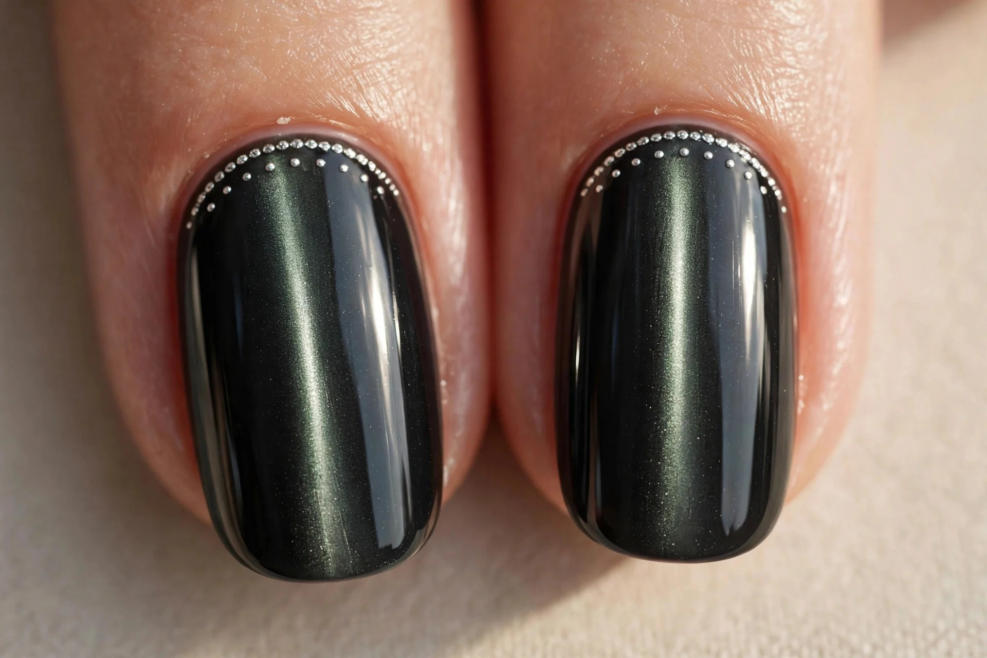 Extreme macro of two fingernails in charcoal black cat-eye gel with a vertical light band, small silver dots tracing a half-m